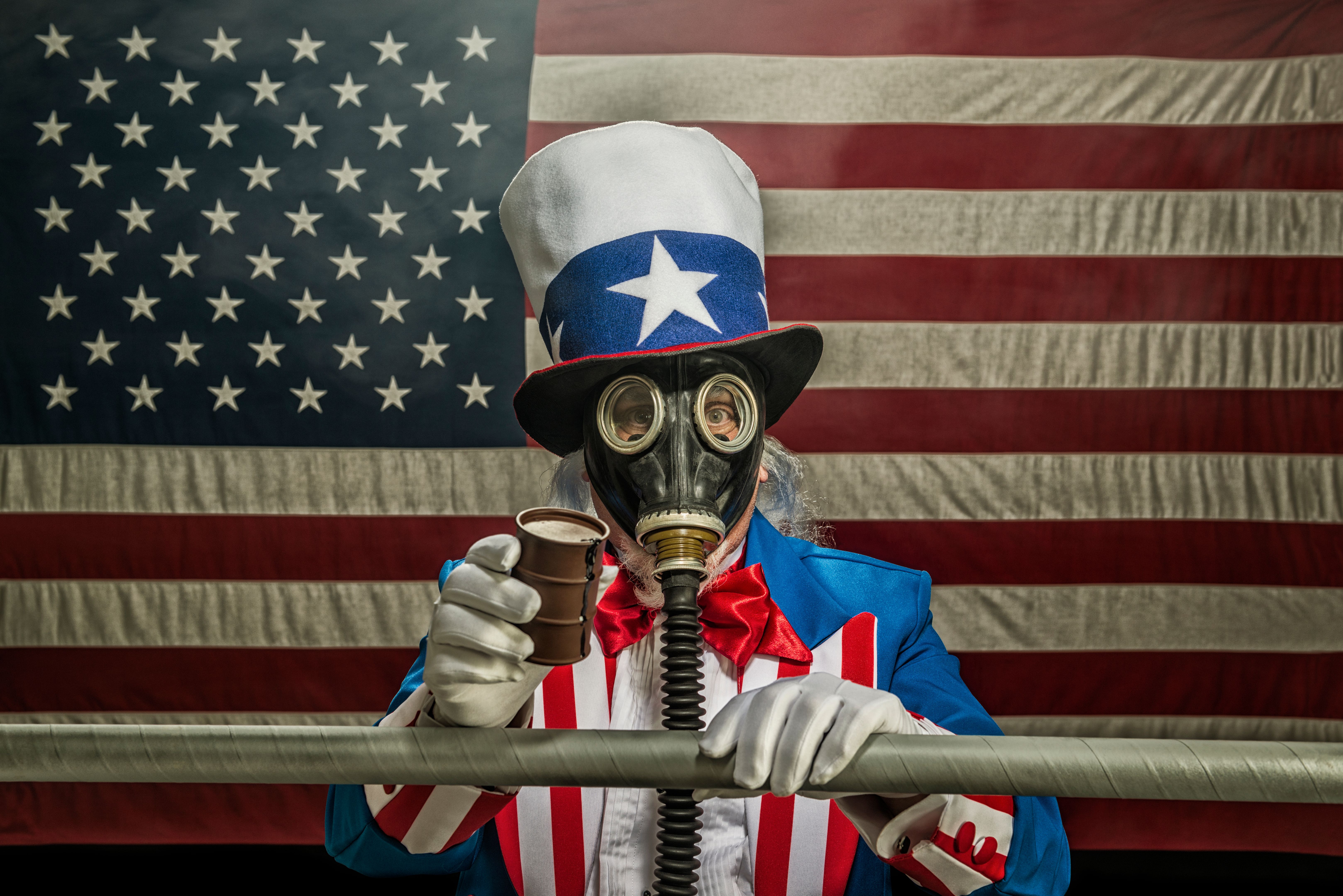 Uncle Sam wearing gas mask holding oil drum and pipe line