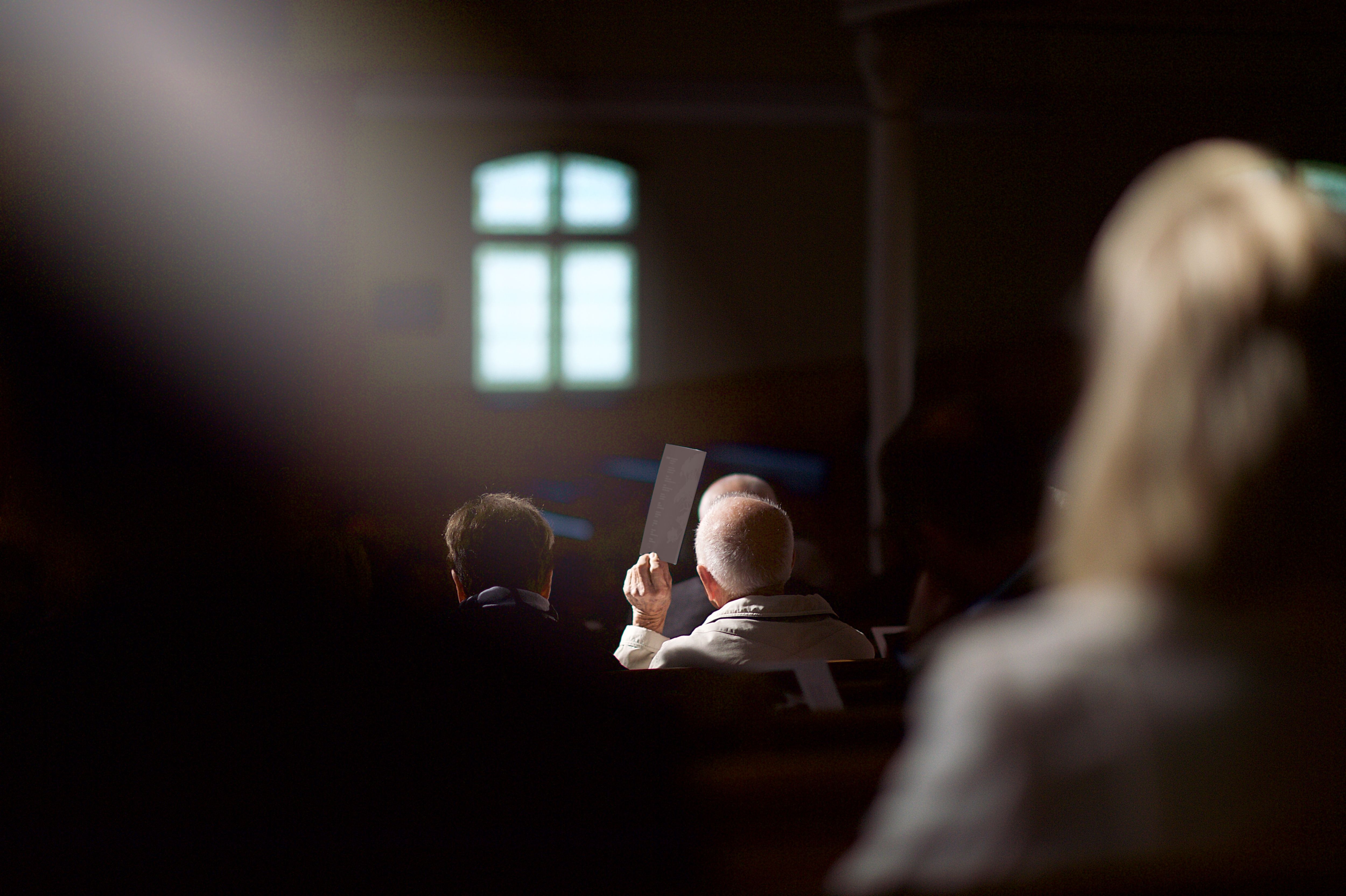 Old couple rear view in church keeping the sunlight beam out of his eyes