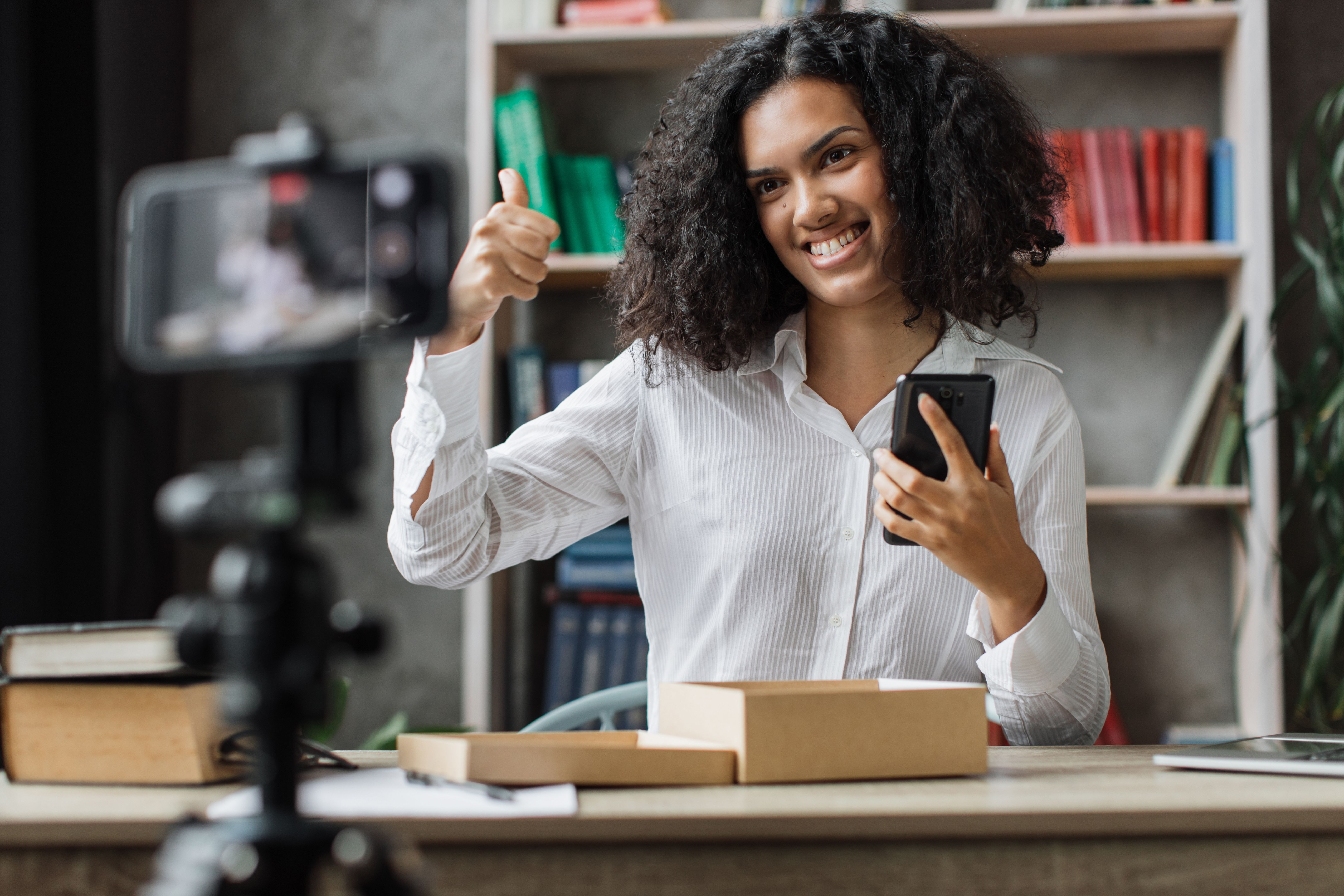 Pleasant multinational woman while opening parcel box with new smartphon