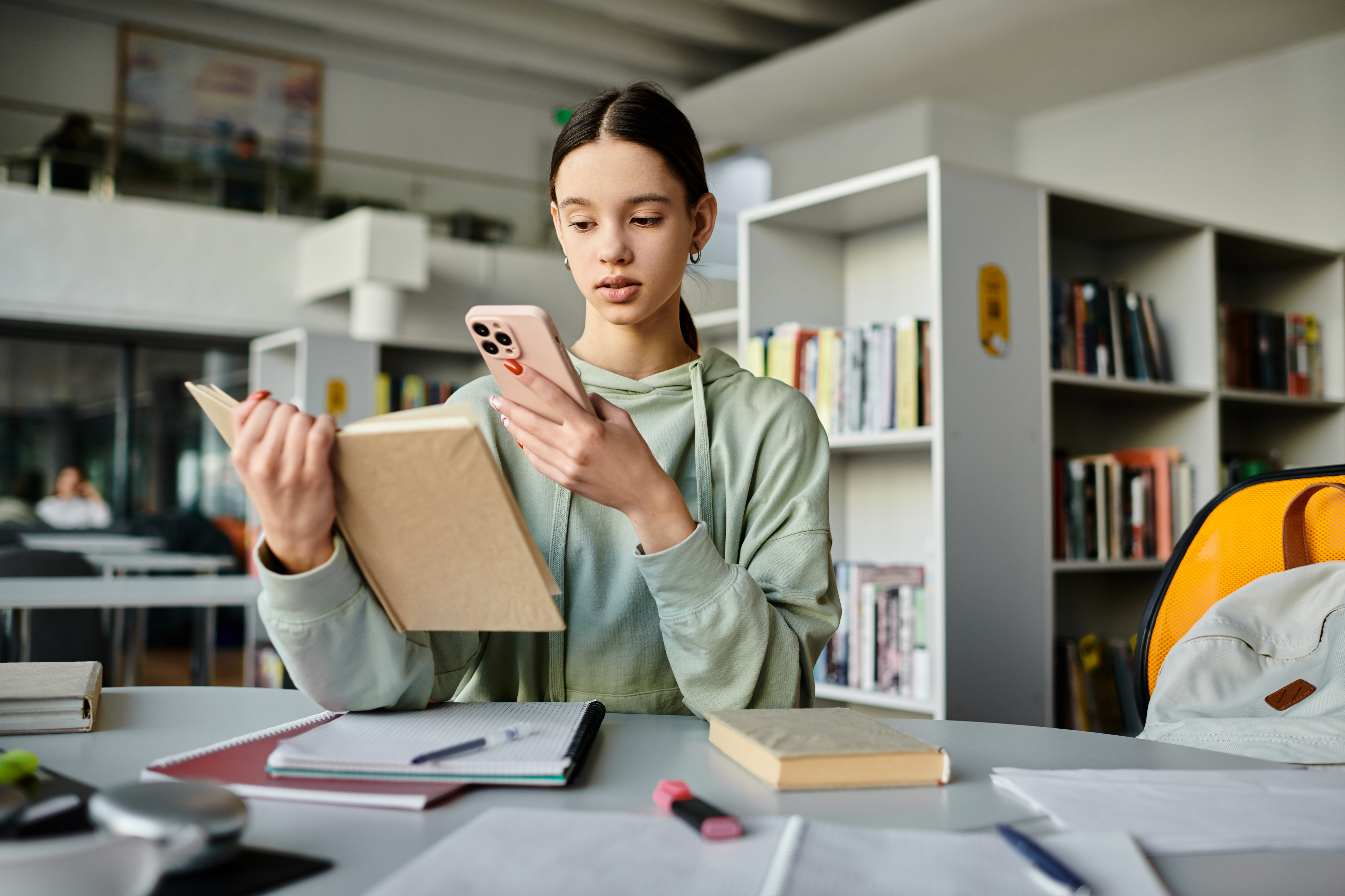 Teen girl studying hard in the library, balancing homework and phone distractions