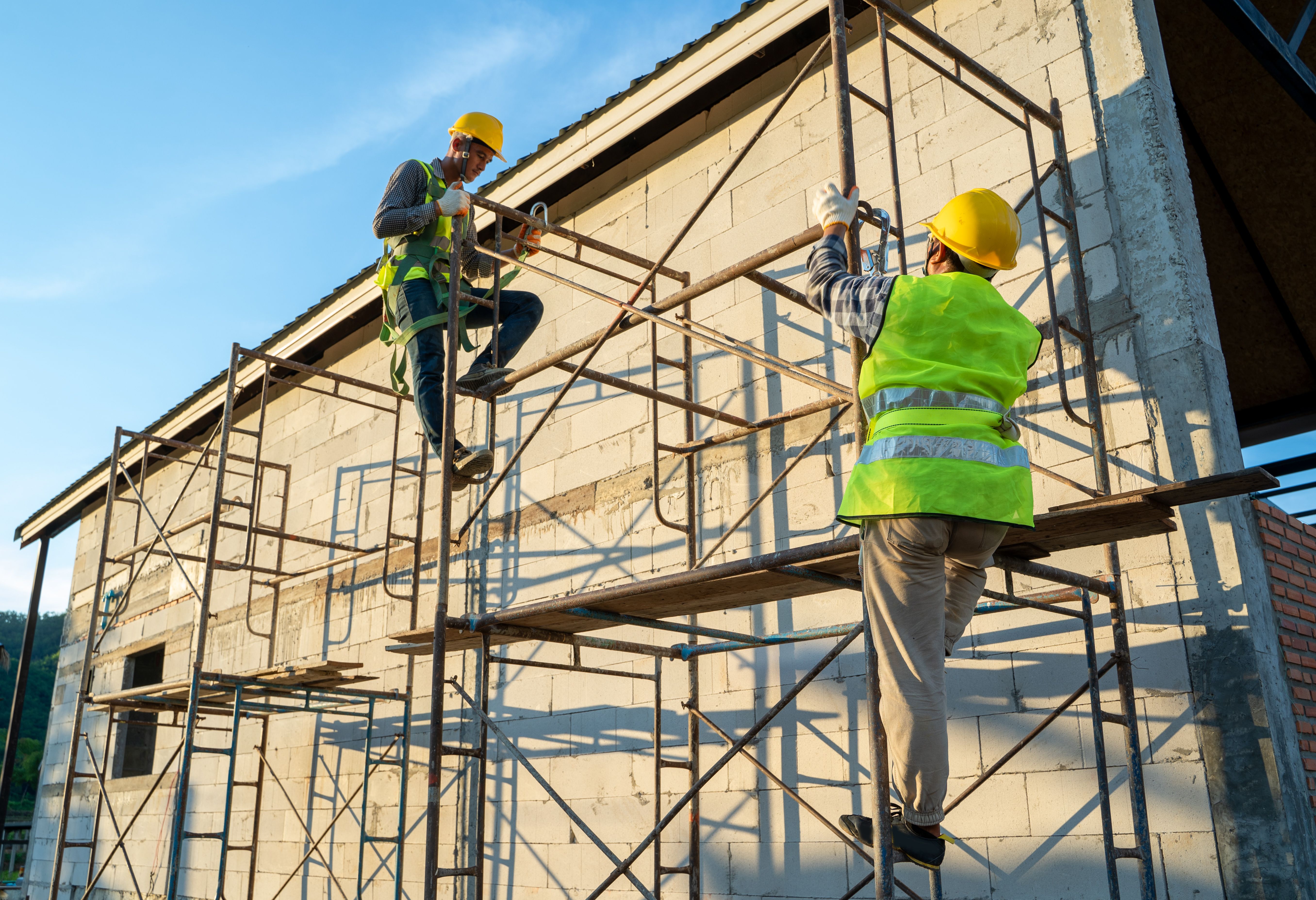 Construction workers in uniform and safety equipment working on scaffolding.