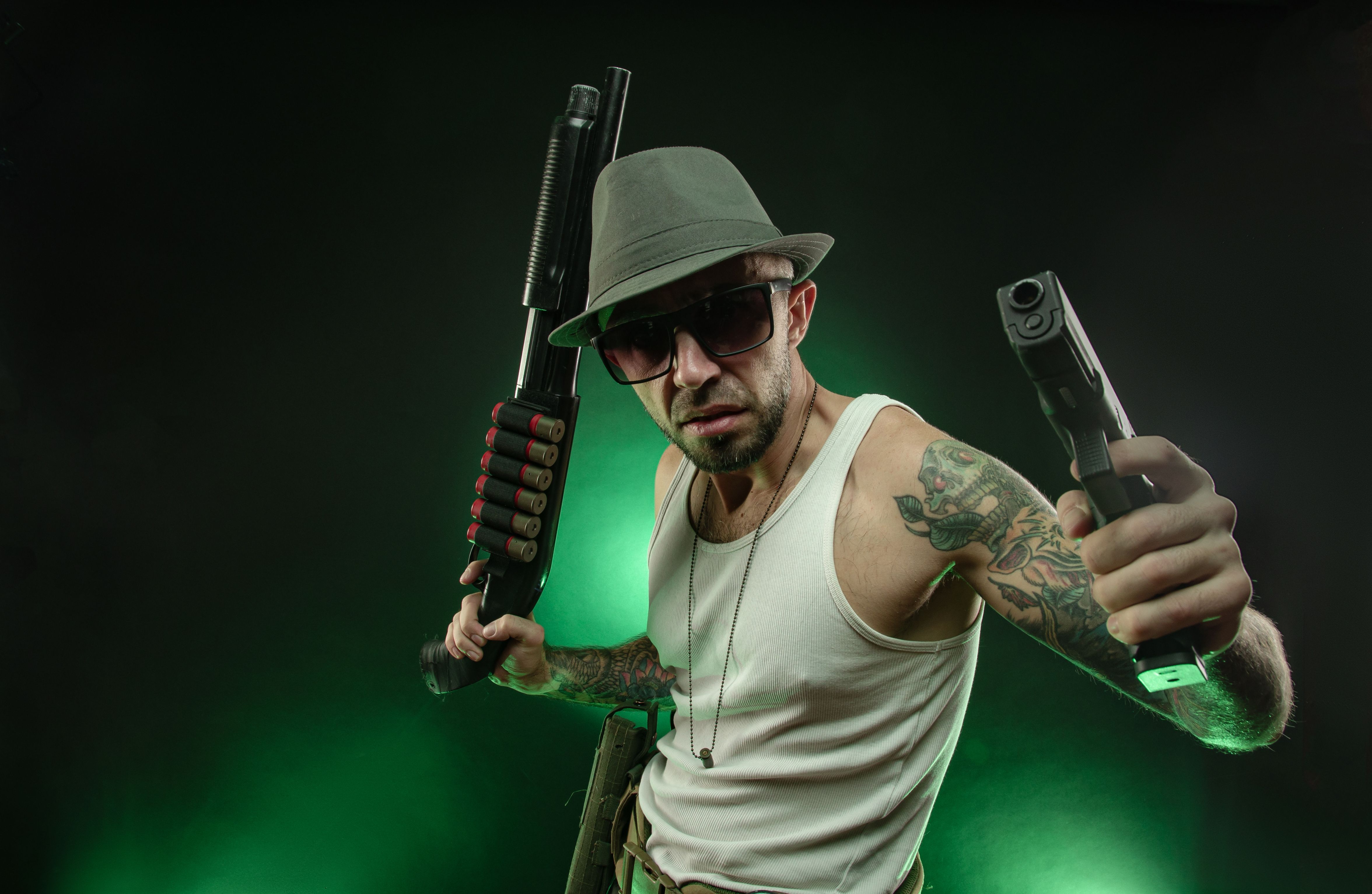 an athletic guy with a tattoo poses with a shotgun