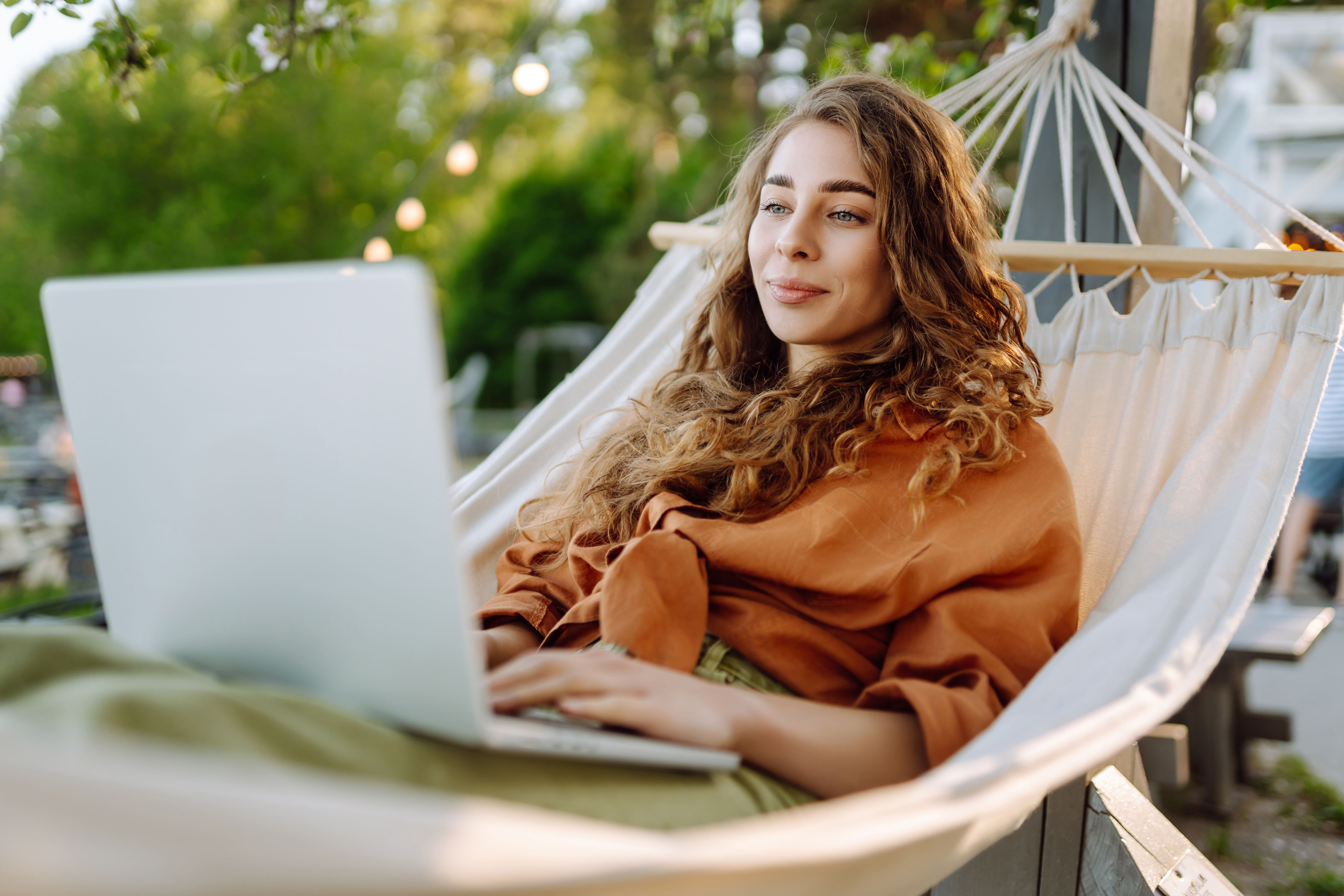 Young woman with laptop working lying in a hammock among trees in the fresh air.