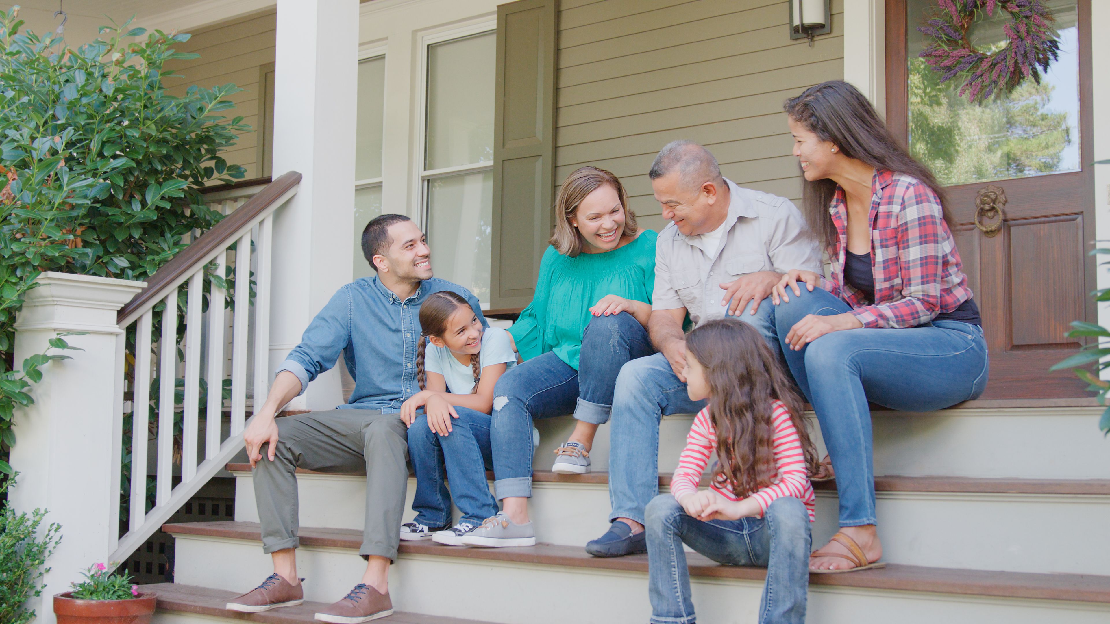 Multi Generation Family Sit On Steps Leading Up To House Porch