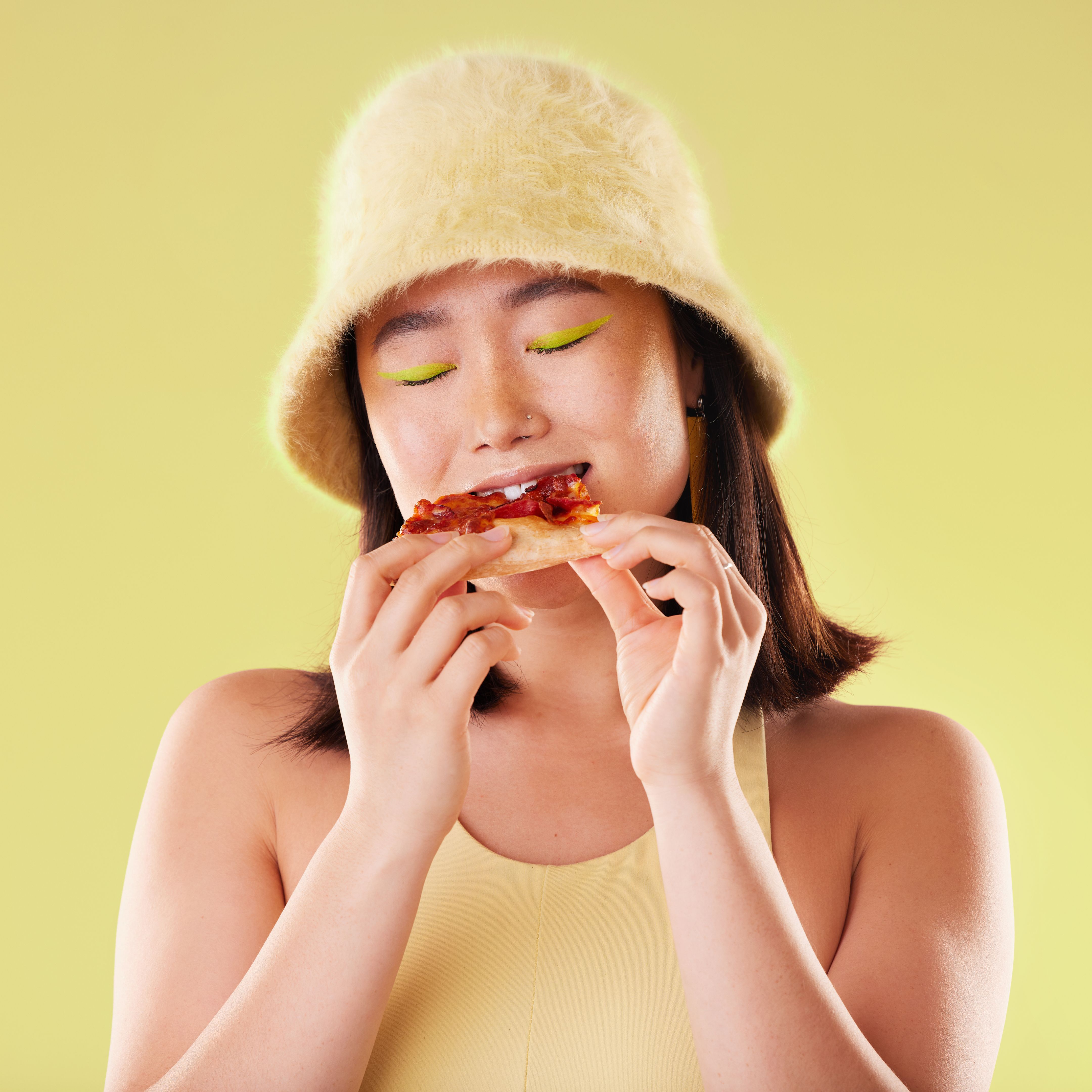 Asian girl, eating pizza and studio with fashion, happiness and retro 90s aesthetic by yellow background. Young gen z model, junk food and happy with meal, cheat snack and beauty with facial makeup Asian girl, eating pizza and studio with fashion, happiness and retro 90s aesthetic by yellow background. Young gen z model, junk food and happy with meal, cheat snack and beauty with facial makeup