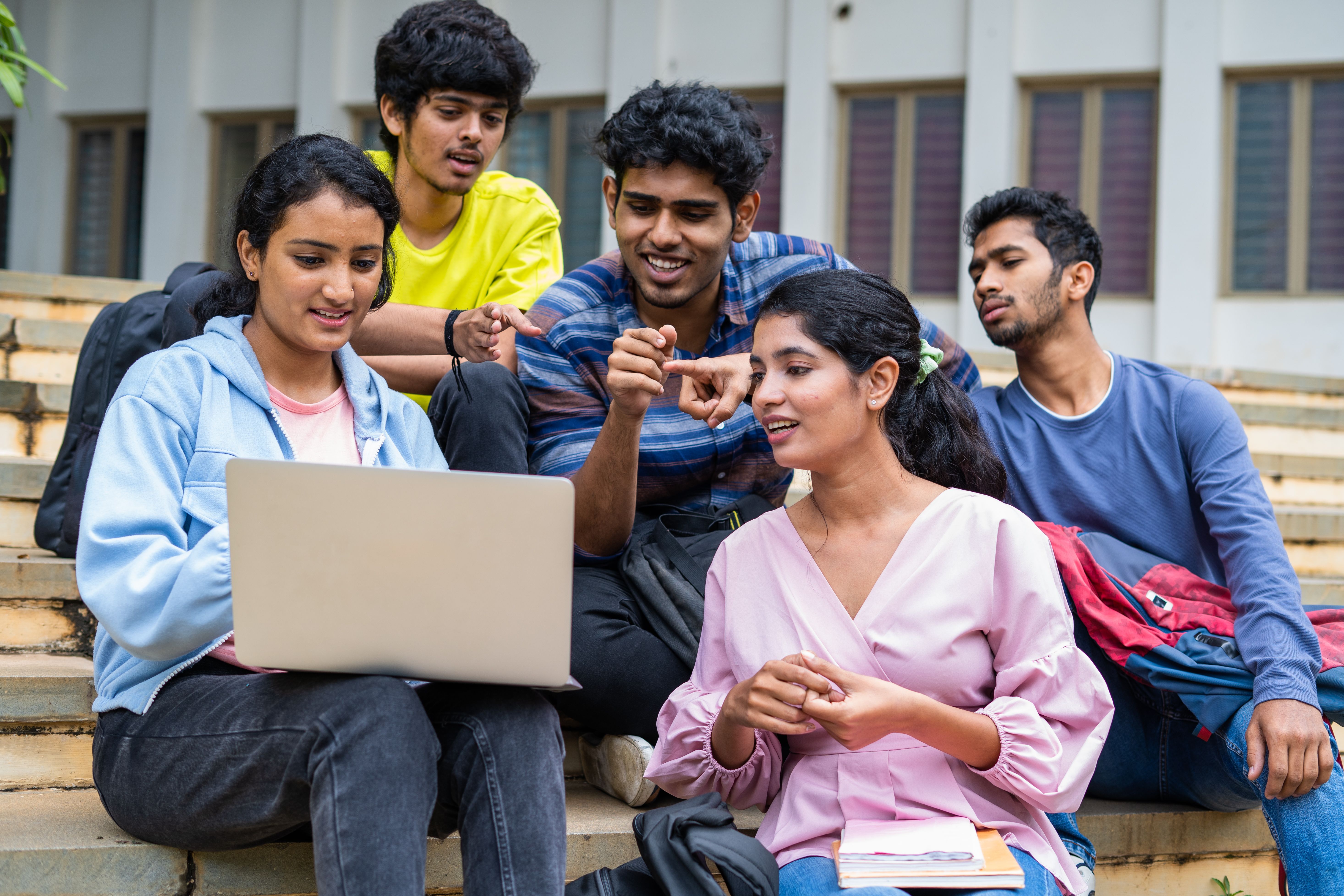 Group of happy students checking results on laptop while sitting on college campus - concept of education, technology and project work discussion. Group of happy students checking results on laptop while sitting on college campus - concept of education, technology and project work discussion.