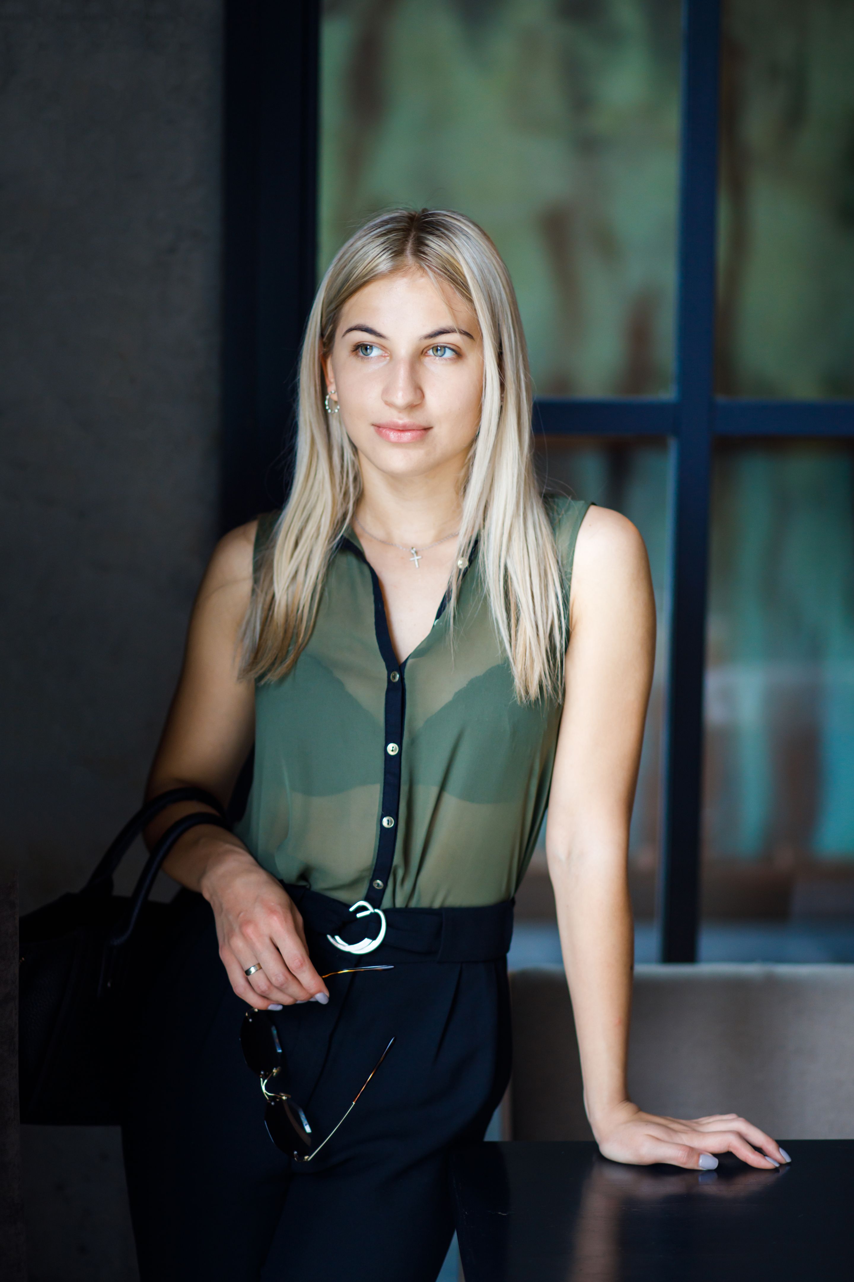 A young beautiful blonde girl stands in a cafe with a bag in her arms. The girl is well dressed, business style. The girl is ready for a business meeting