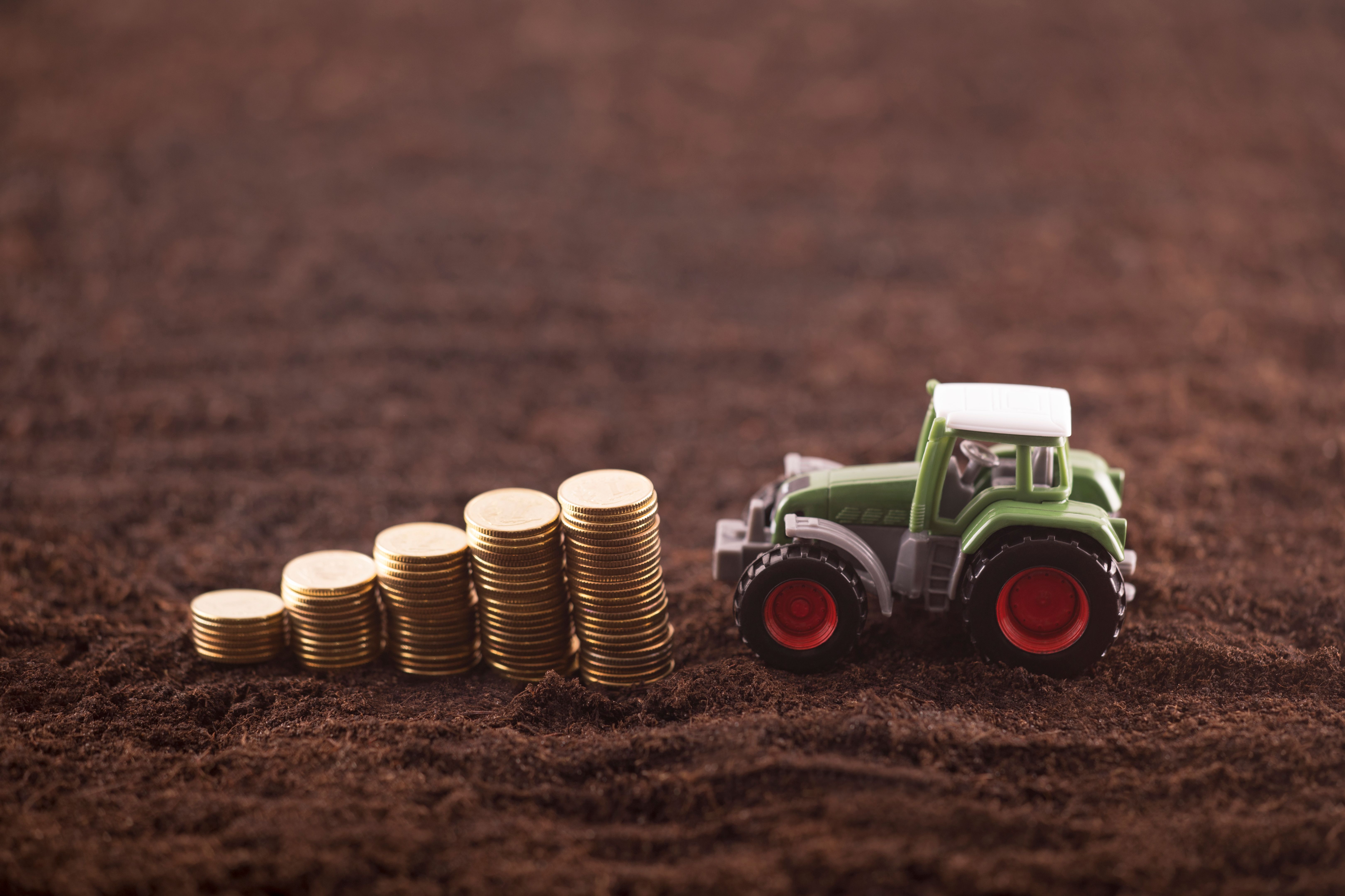 Tractor miniature with coins on fertile soil land Tractor miniature with coins on fertile soil land