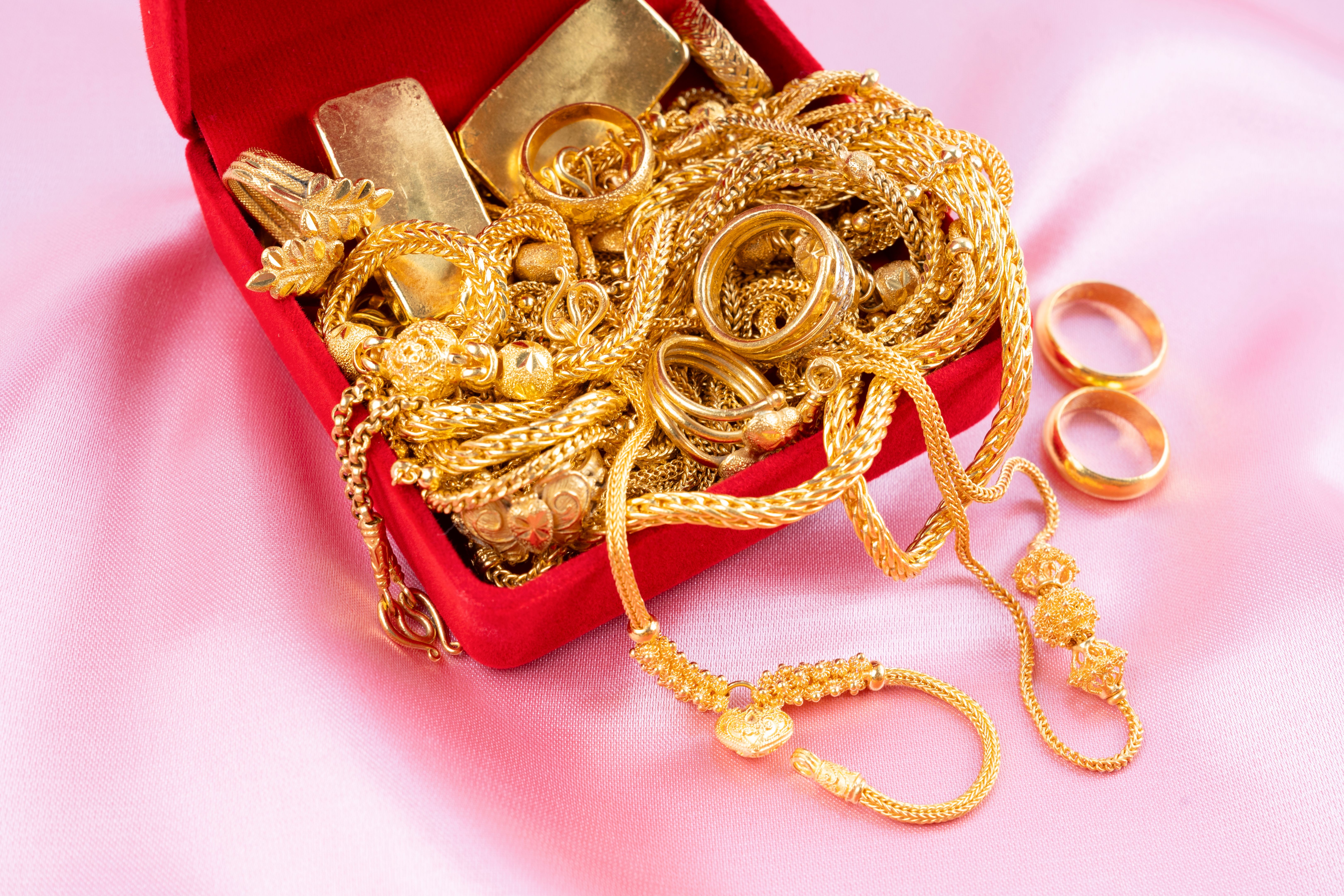 Gold Necklace and rings in red velvet box container on pink color fabric background.