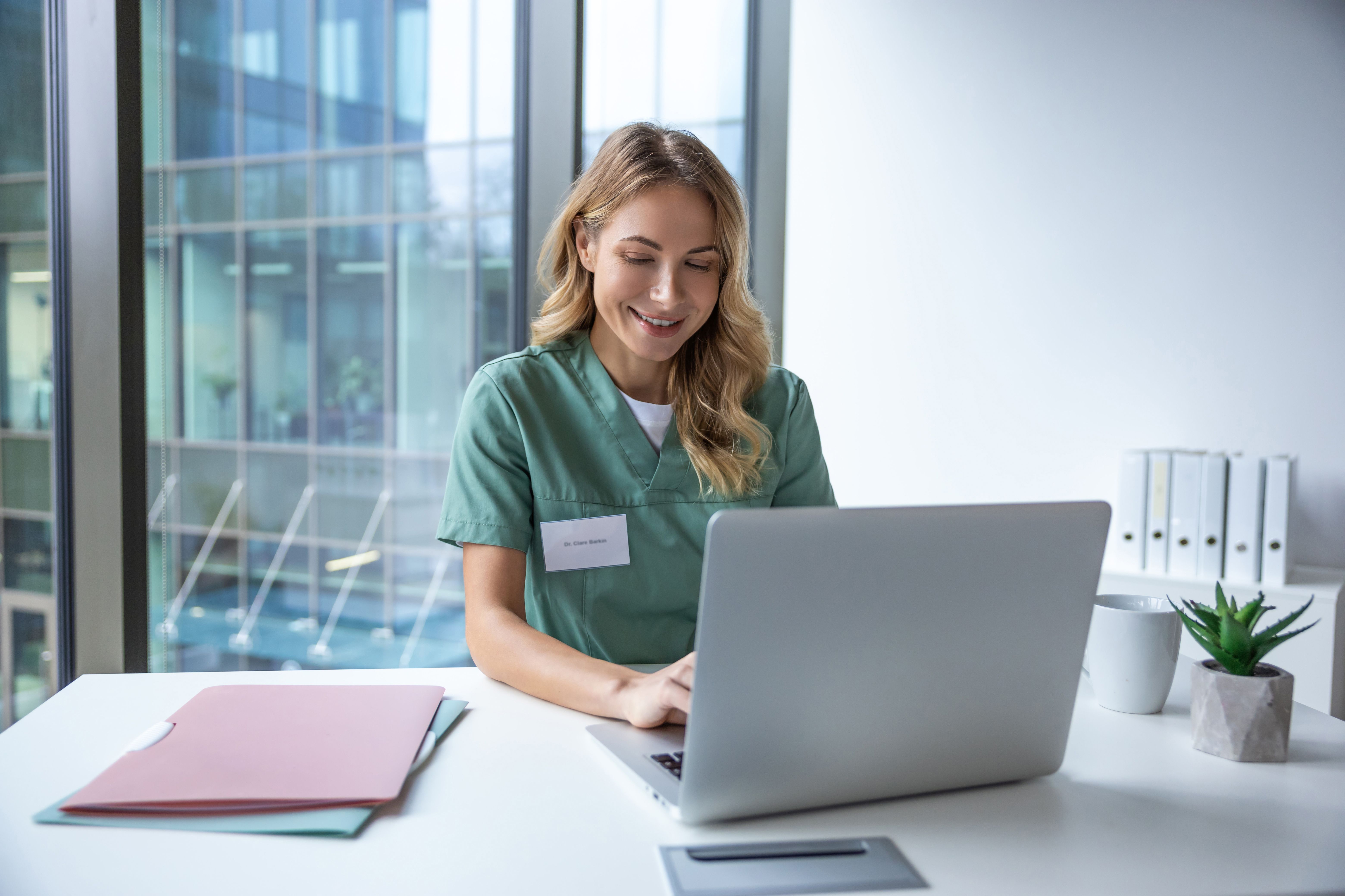 Female doctor in uniform sitting in hospital office working on laptop