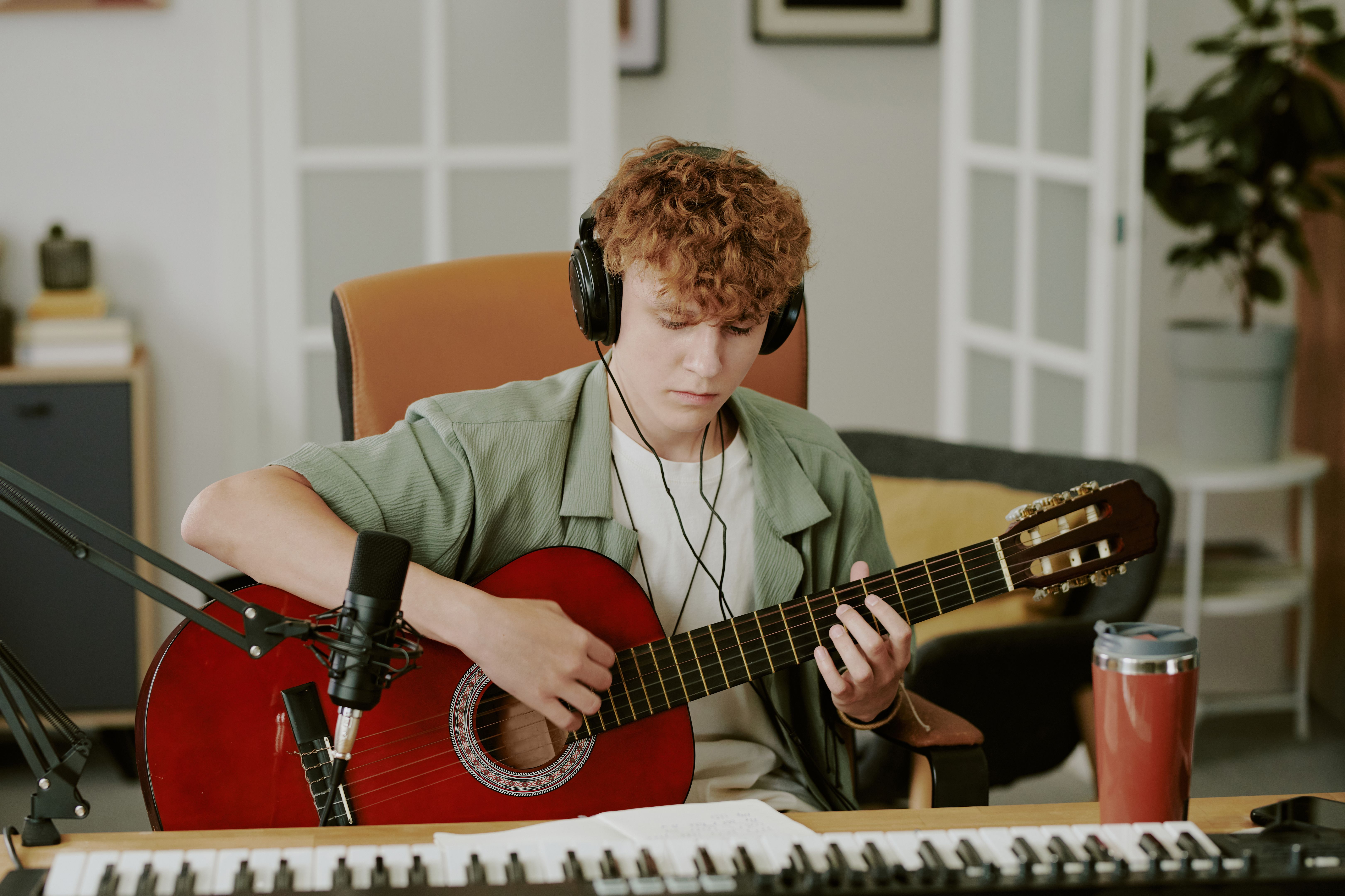 Caucasian Teenager Boy Playing Acoustic Guitar While Recording Music at Home