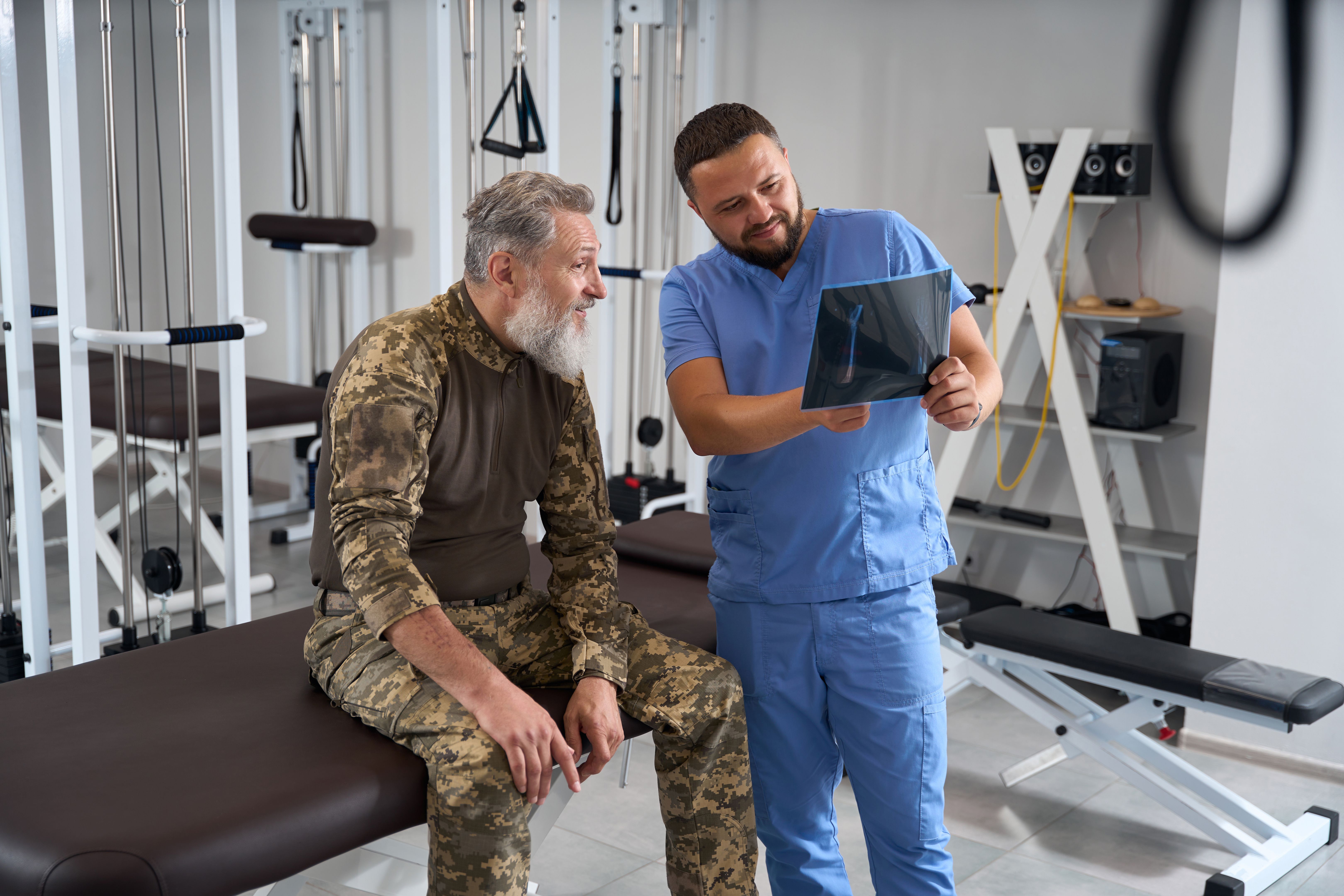 Physiotherapist with a patient in military clothing examines x-rays