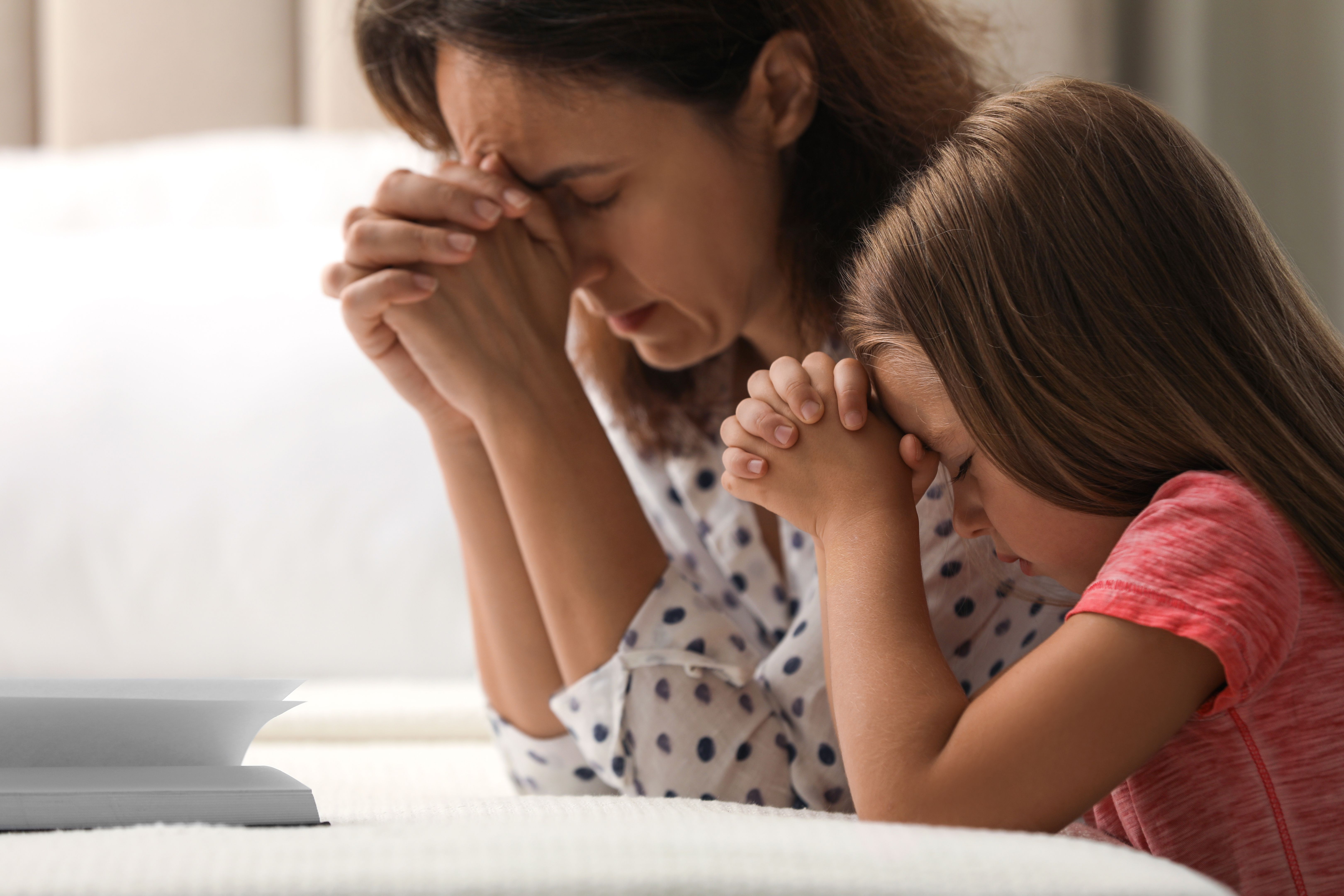 Mature woman with her little granddaughter praying together over Bible in bedroom Mature woman with her little granddaughter praying together over Bible in bedroom