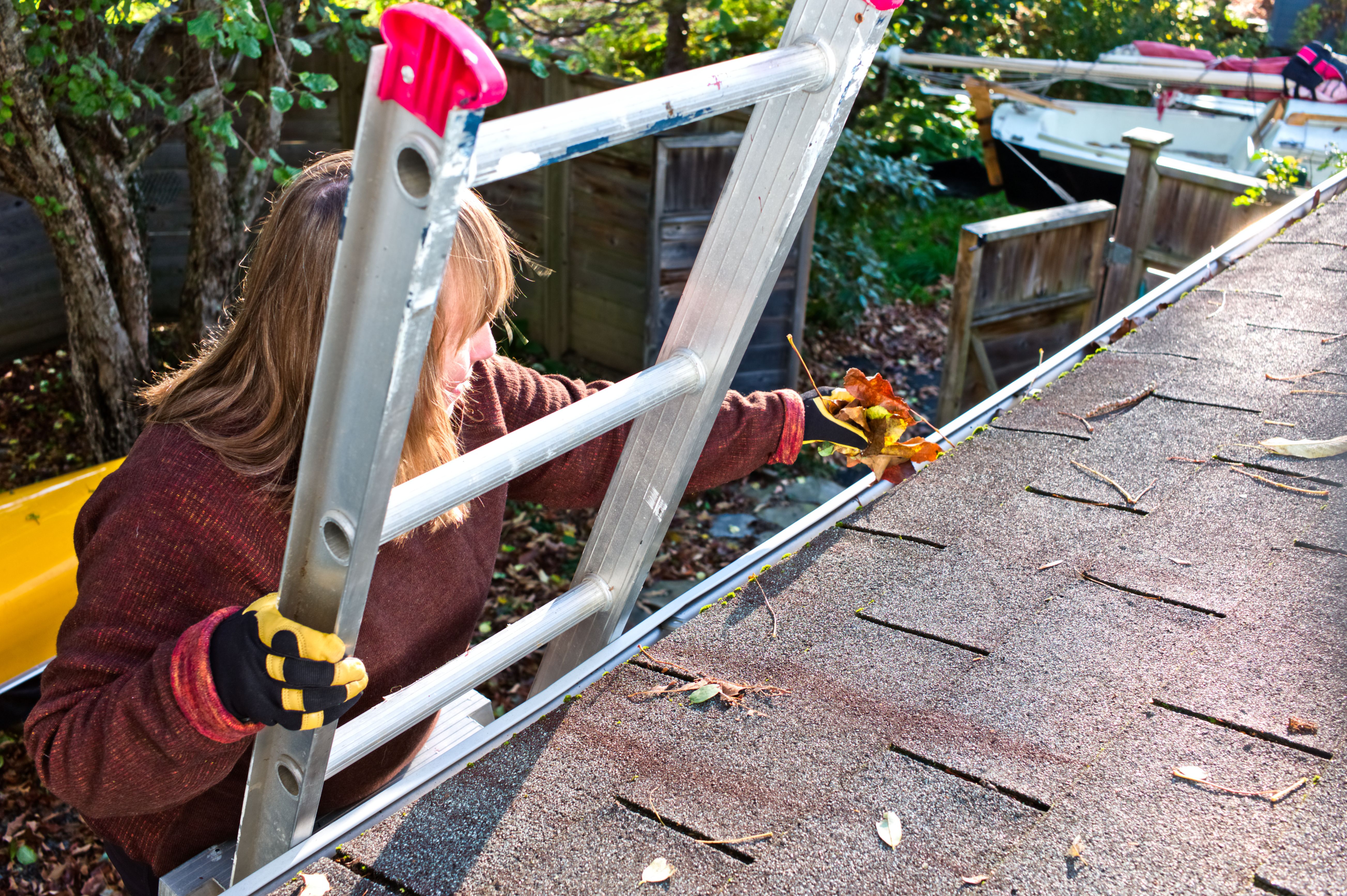 Mature woman on a ladder cleaning gutters of leaves. Mature woman on a ladder cleaning gutters of leaves.