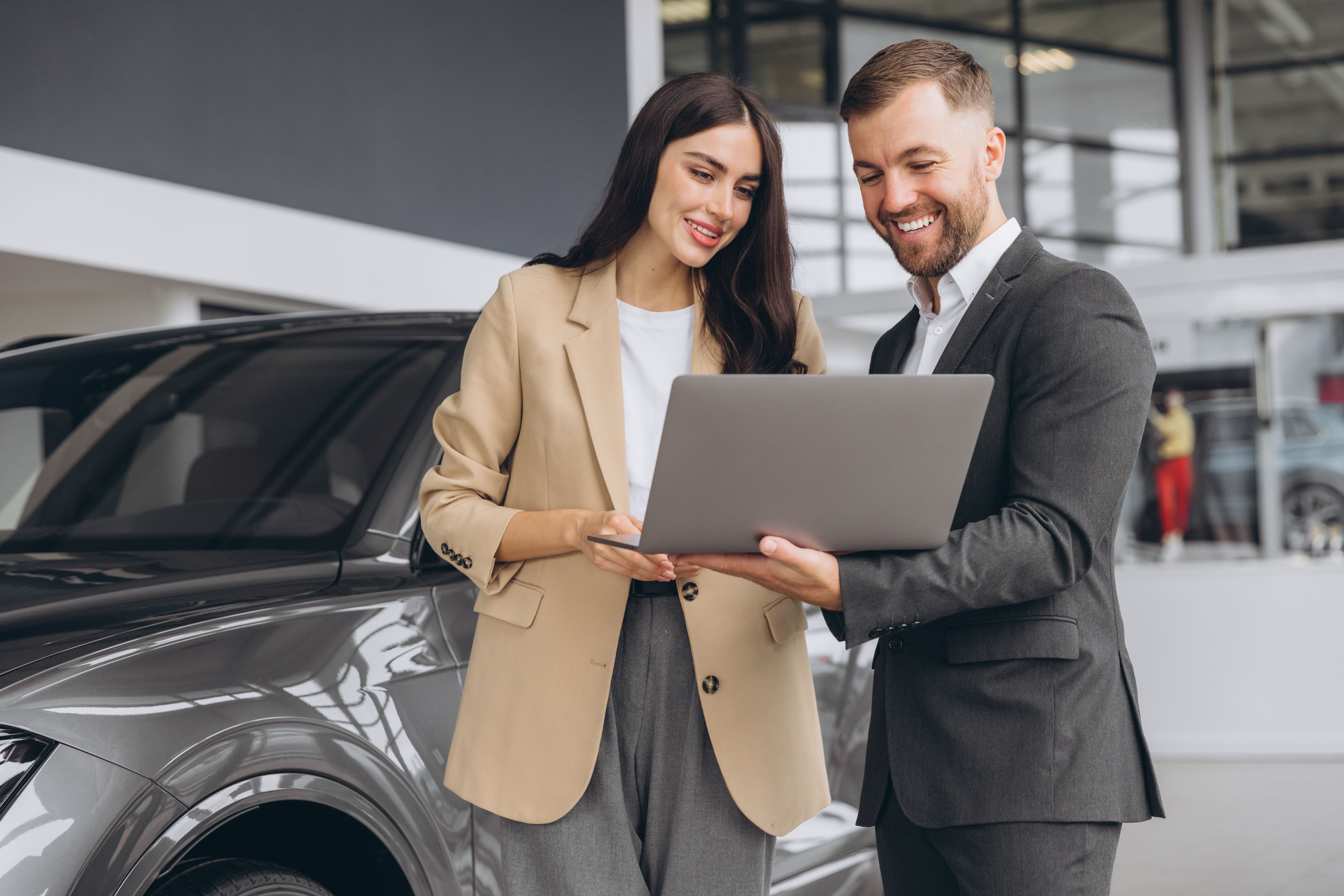Male car salesman, recommends a car to a woman buyer, inspects cars in the showroom, the seller uses a laptop to view technical information on the car
