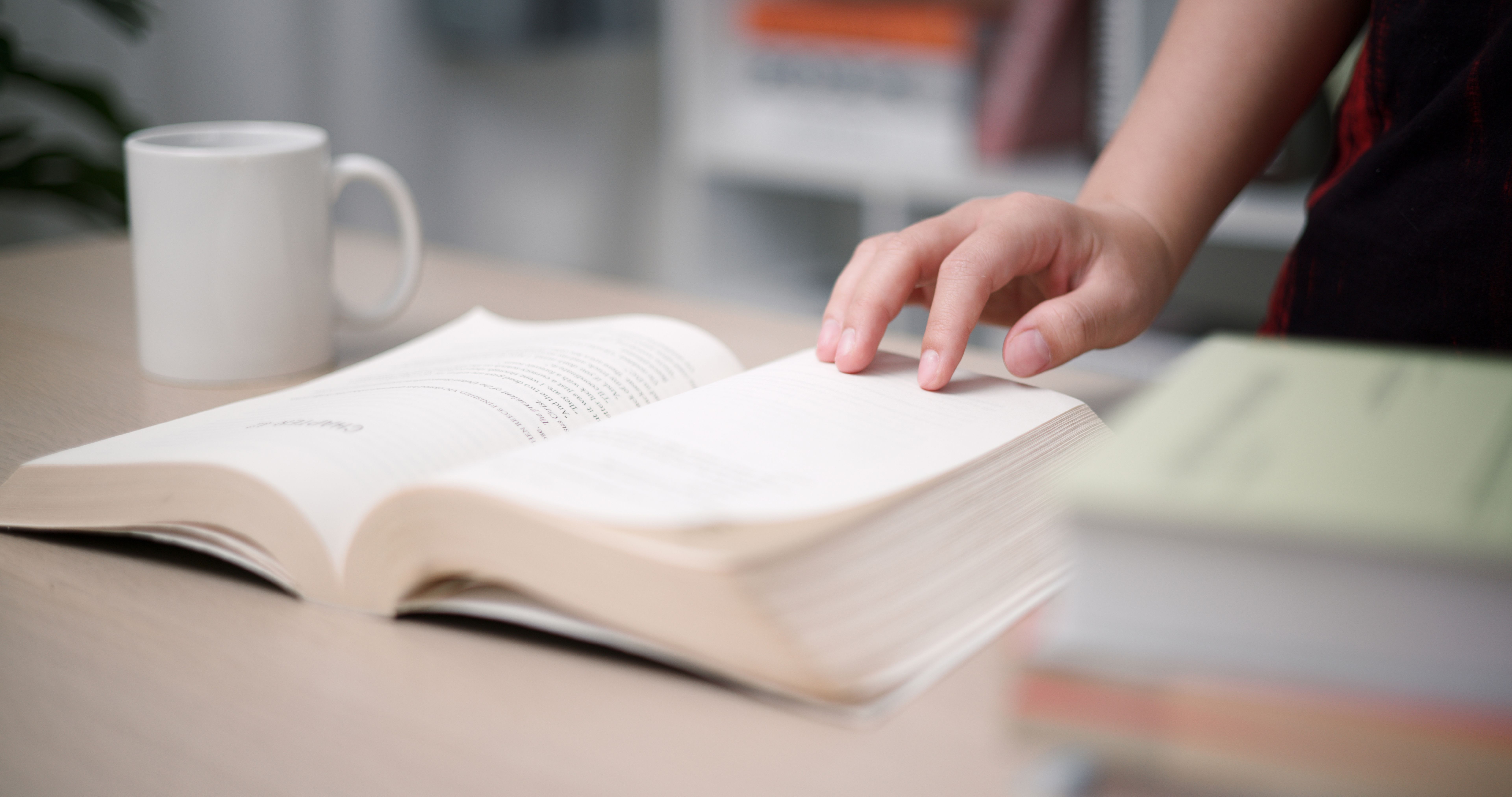 Woman hand turns the pages of book and reading a book on wood table in home.