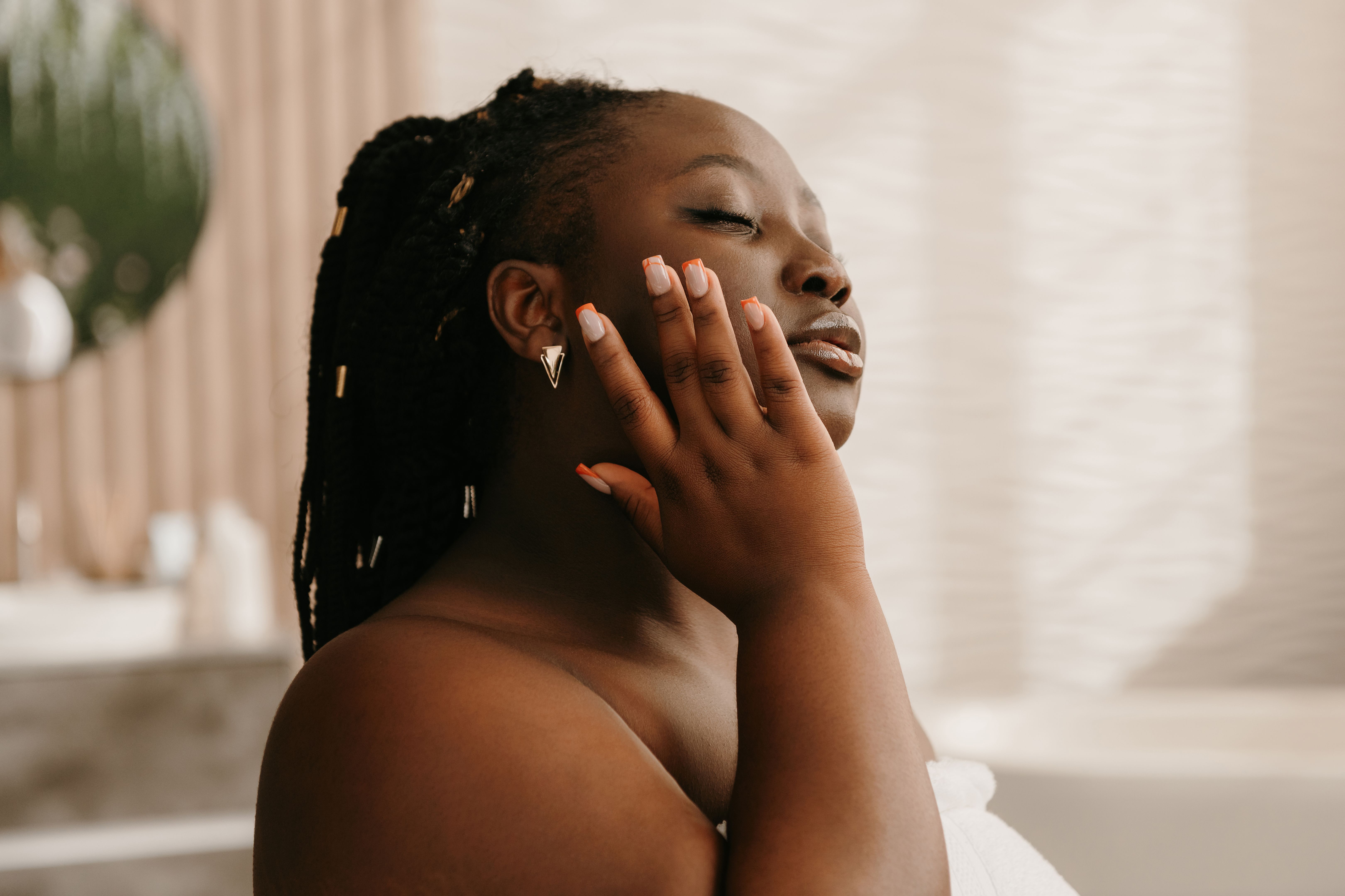 Confident curvy African woman covered in towel applying hydrating face cream in bathroom Confident curvy African woman covered in towel applying hydrating face cream in bathroom