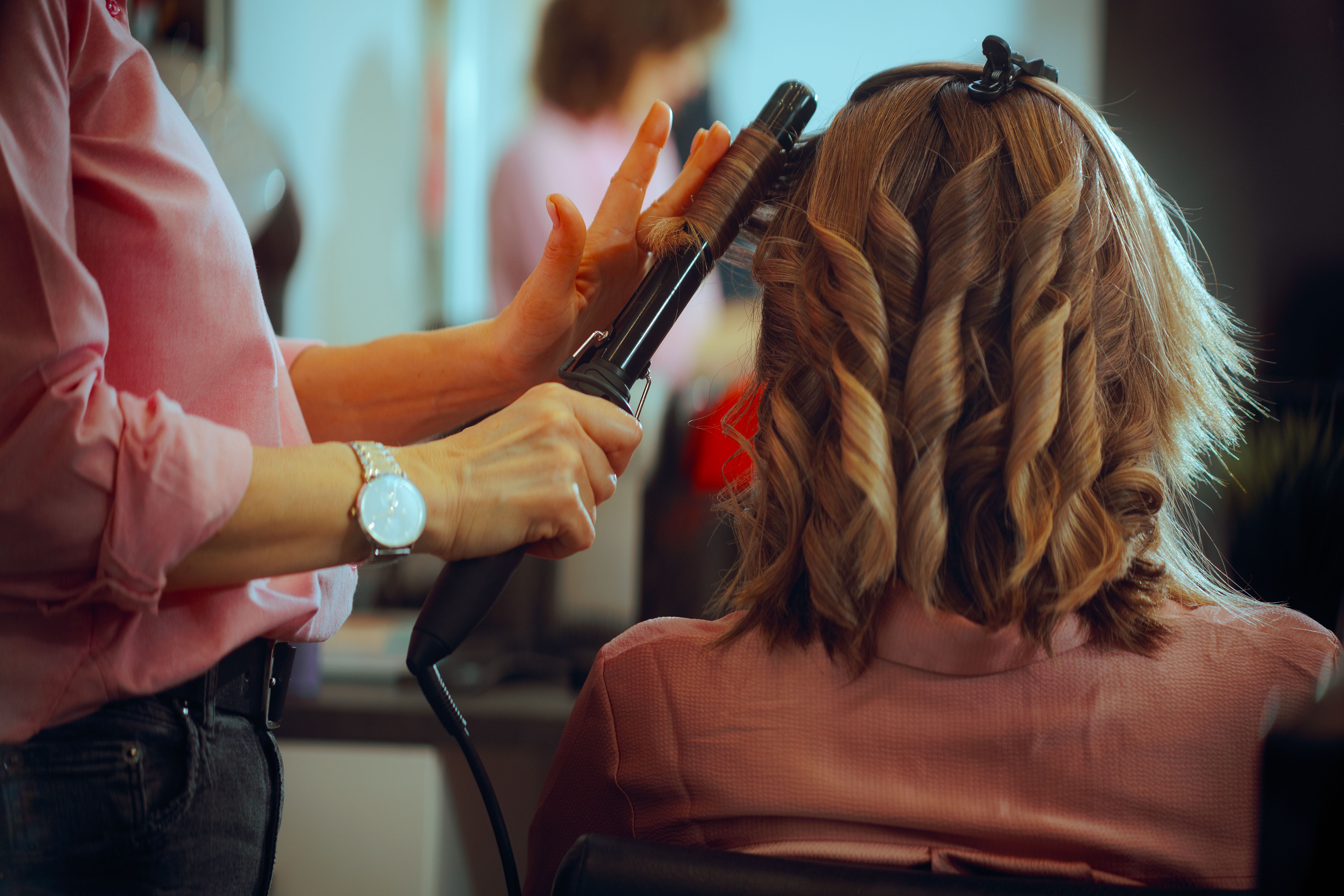 Hairdresser is Curling Hair of a Client using Hair Straightener