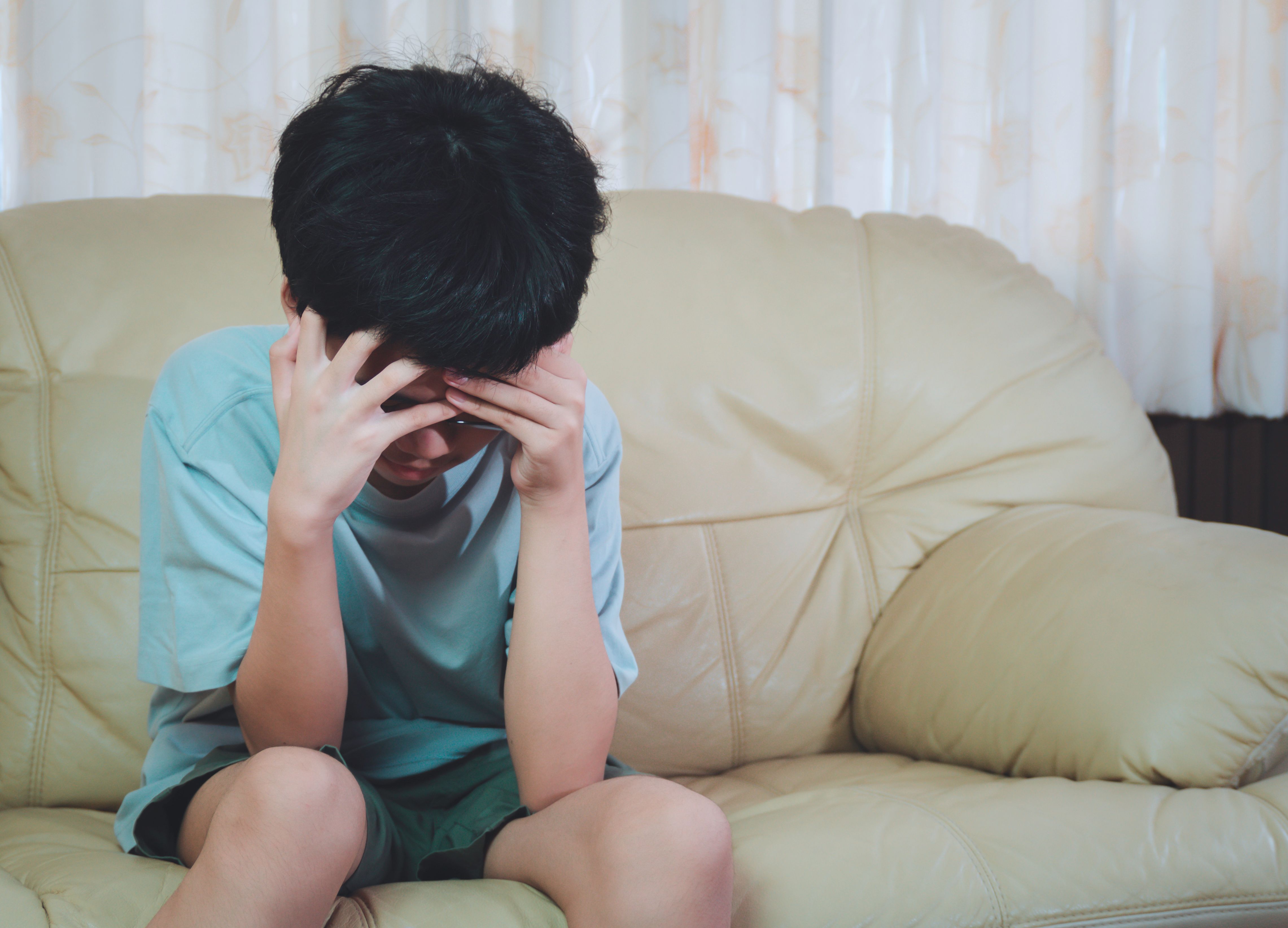 Little asia boy wearing glasses with hand on head, headache because stress. He sad with suffering migraine.