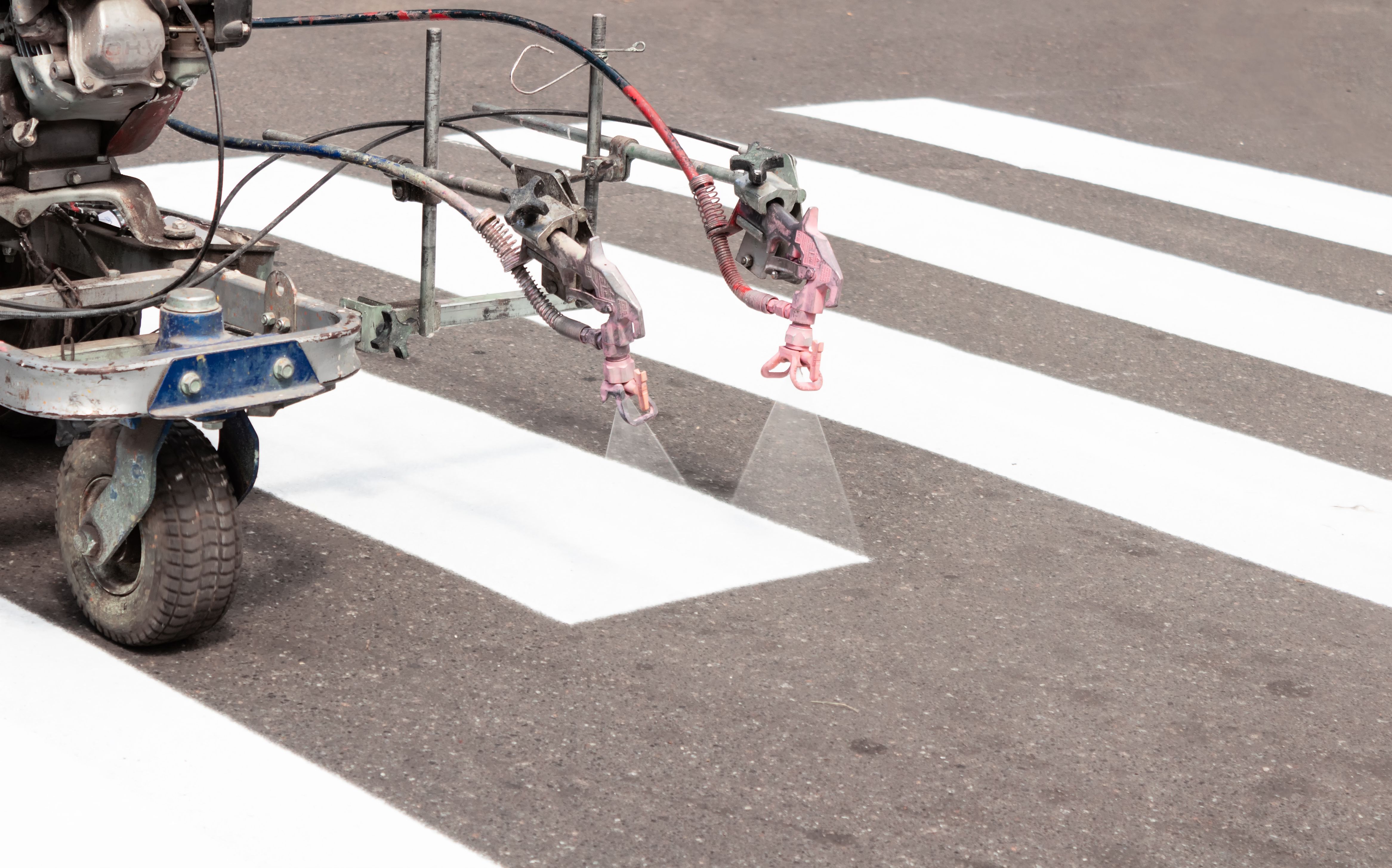 City workers paint crosswalk lanes on the road with painting machine. Close up. City workers paint crosswalk lanes on the road with painting machine. Close up.