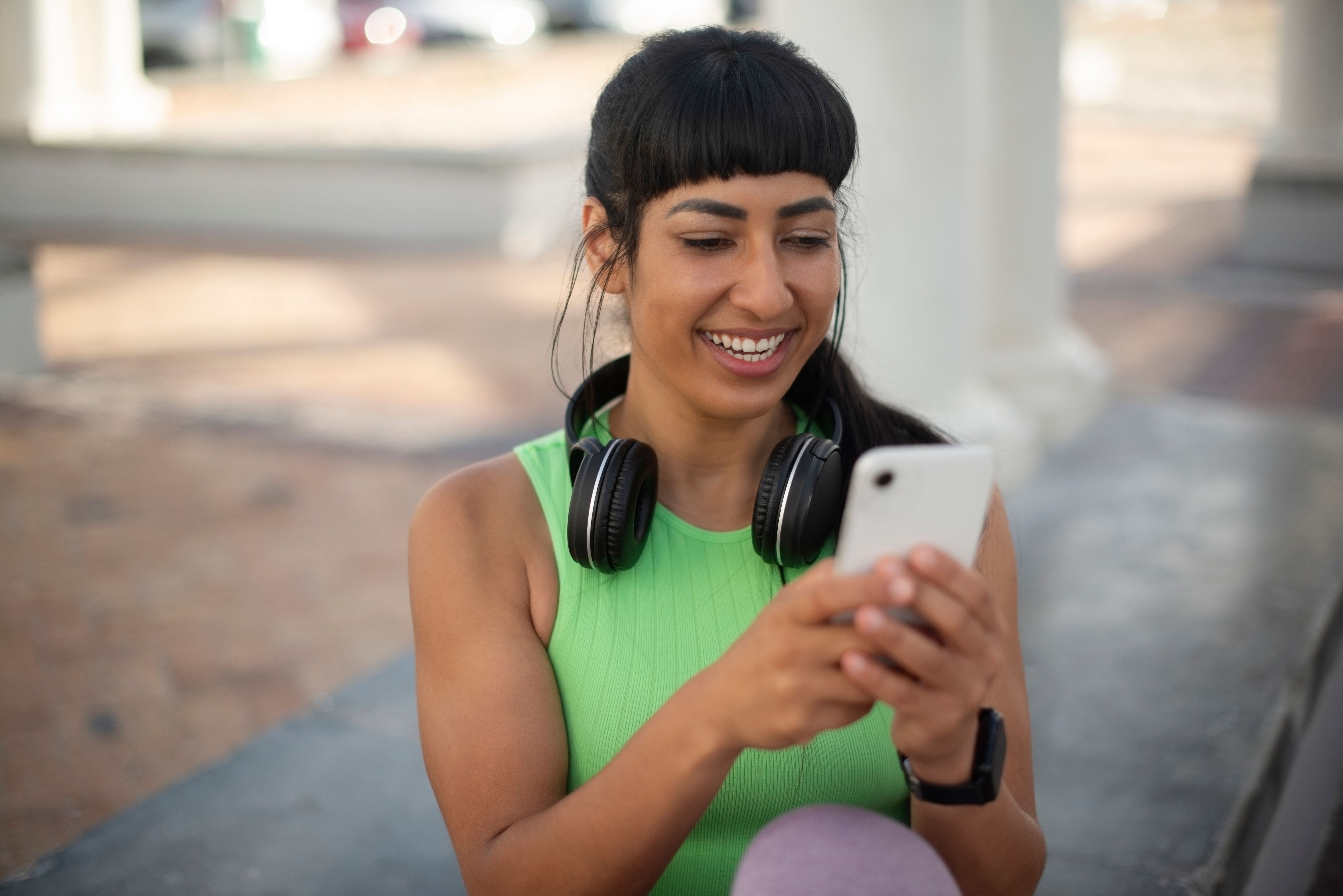 Fitness, woman and typing with phone outdoor for running break, text message response or watching workout video. Space, headphones and girl with smartphone for health mobile app or streaming service