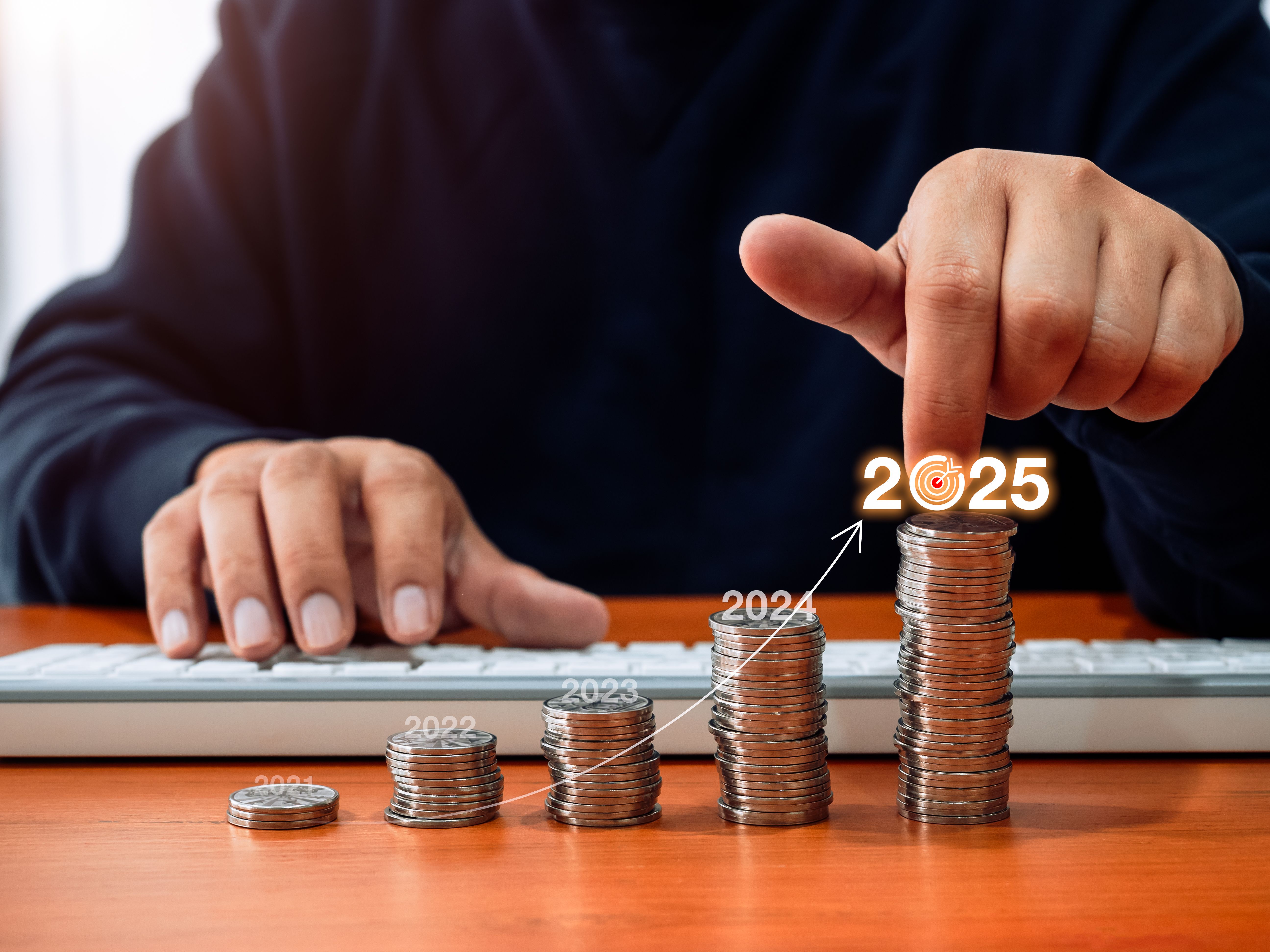 Happy new year 2025, business growth, investment, profit, savings money concept. Rise arrow on 2025 number on coin stacks as graph step, pointing by businessman hand while calculated with computer.