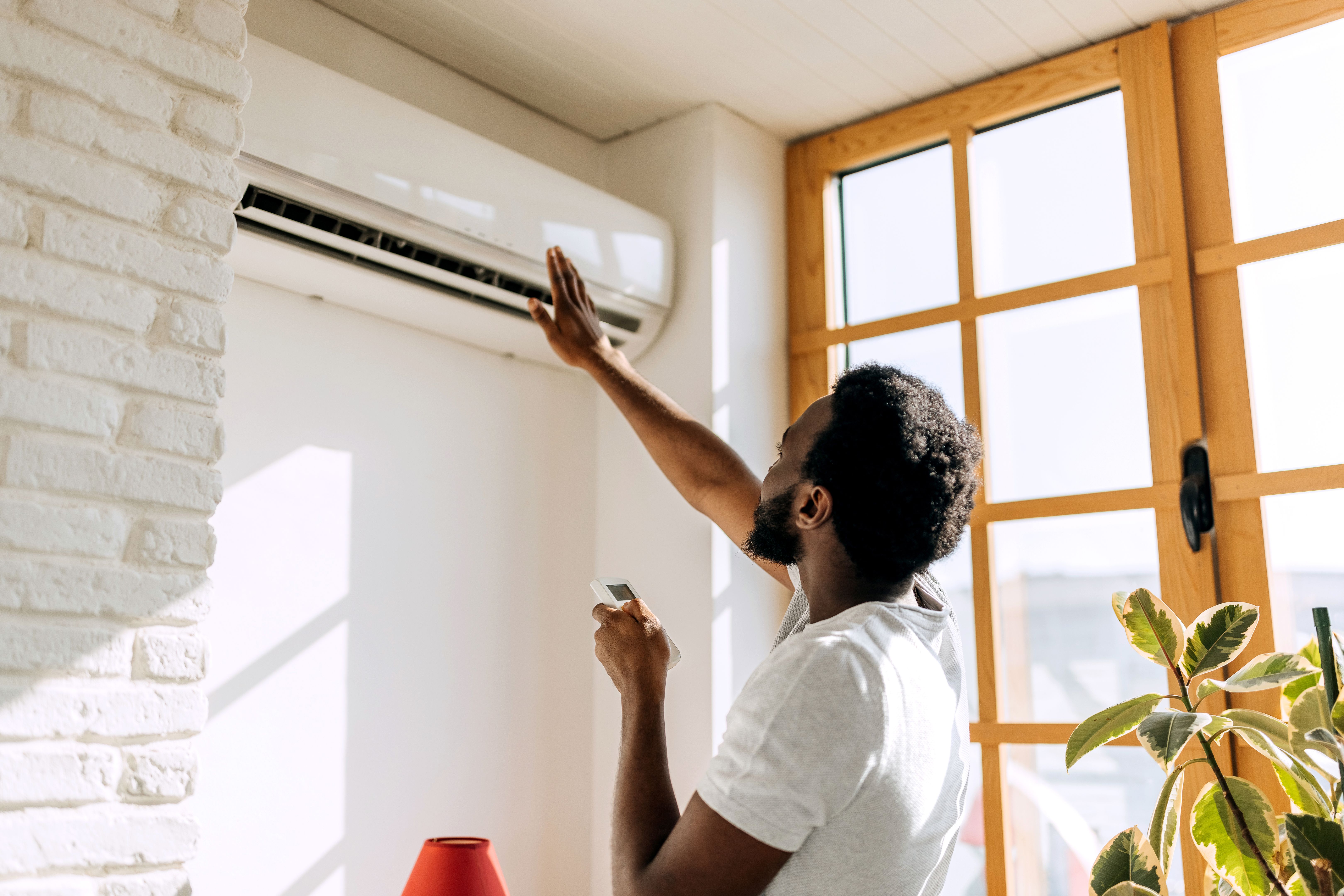 Rear view of young man turning on air conditioner