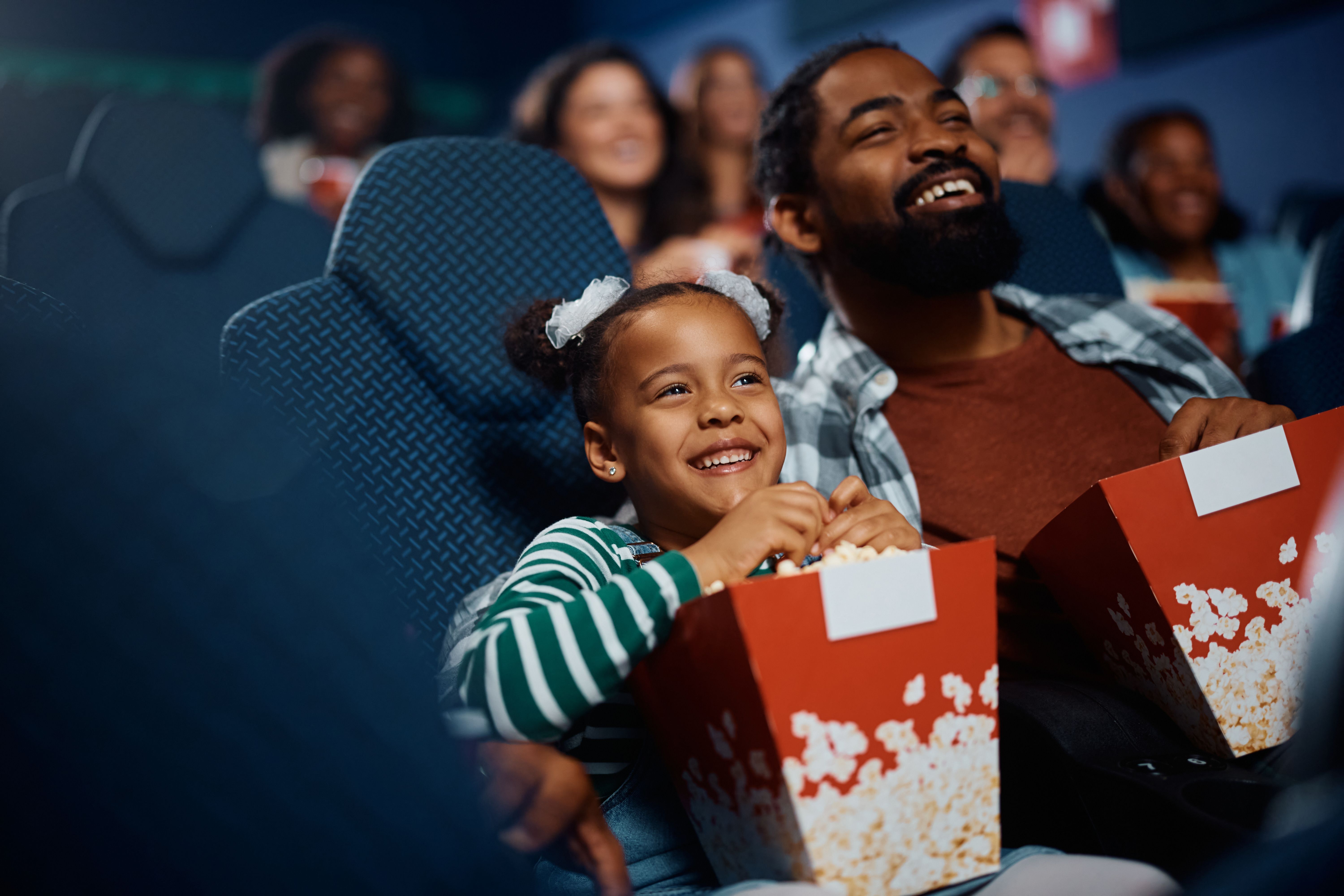 Happy black father and daughter enjoying in movie projection in theater. Happy black father and daughter enjoying in movie projection in theater.