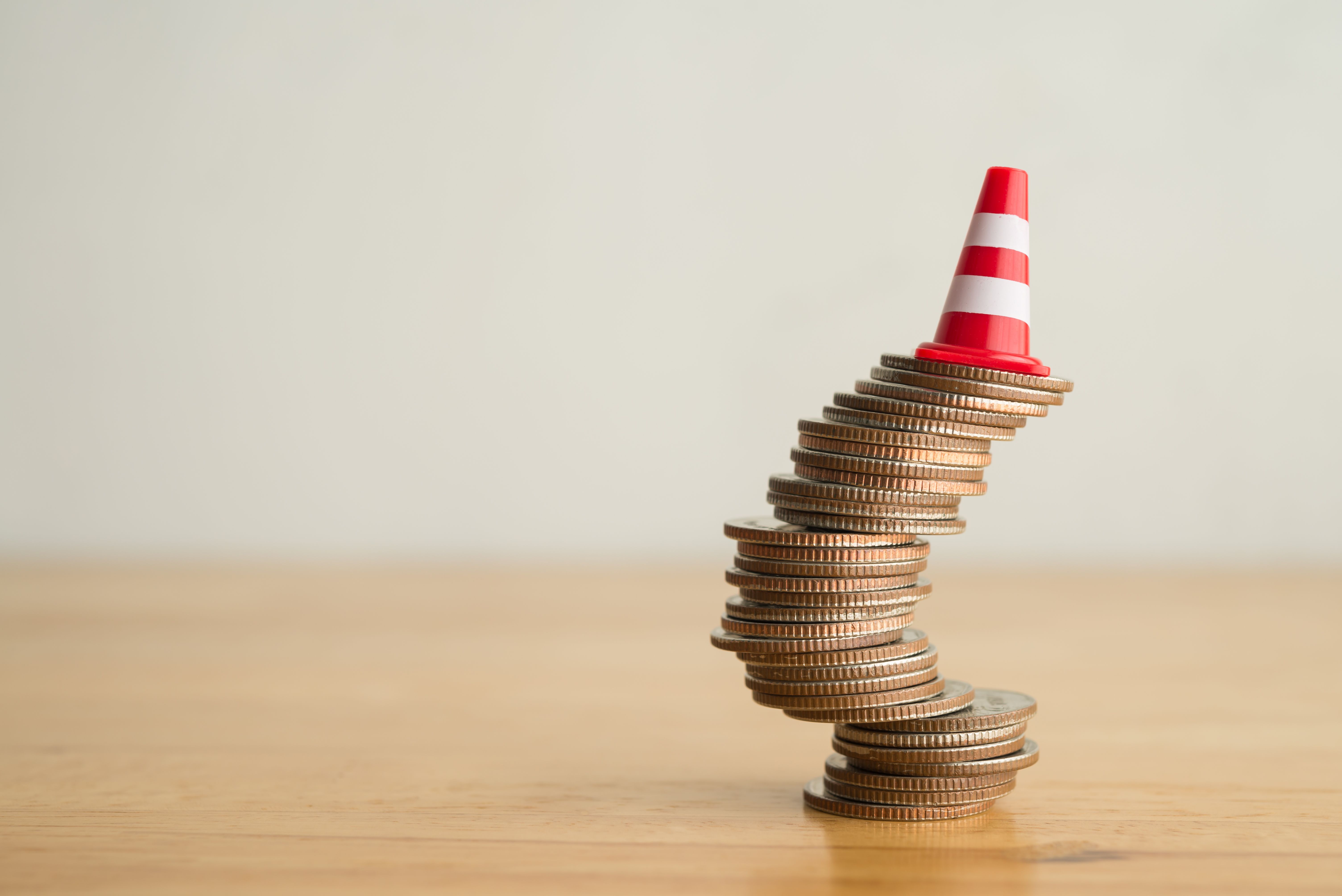 Red traffic cone on stack coins in uncertainty situation on wooden table with white background copy space.