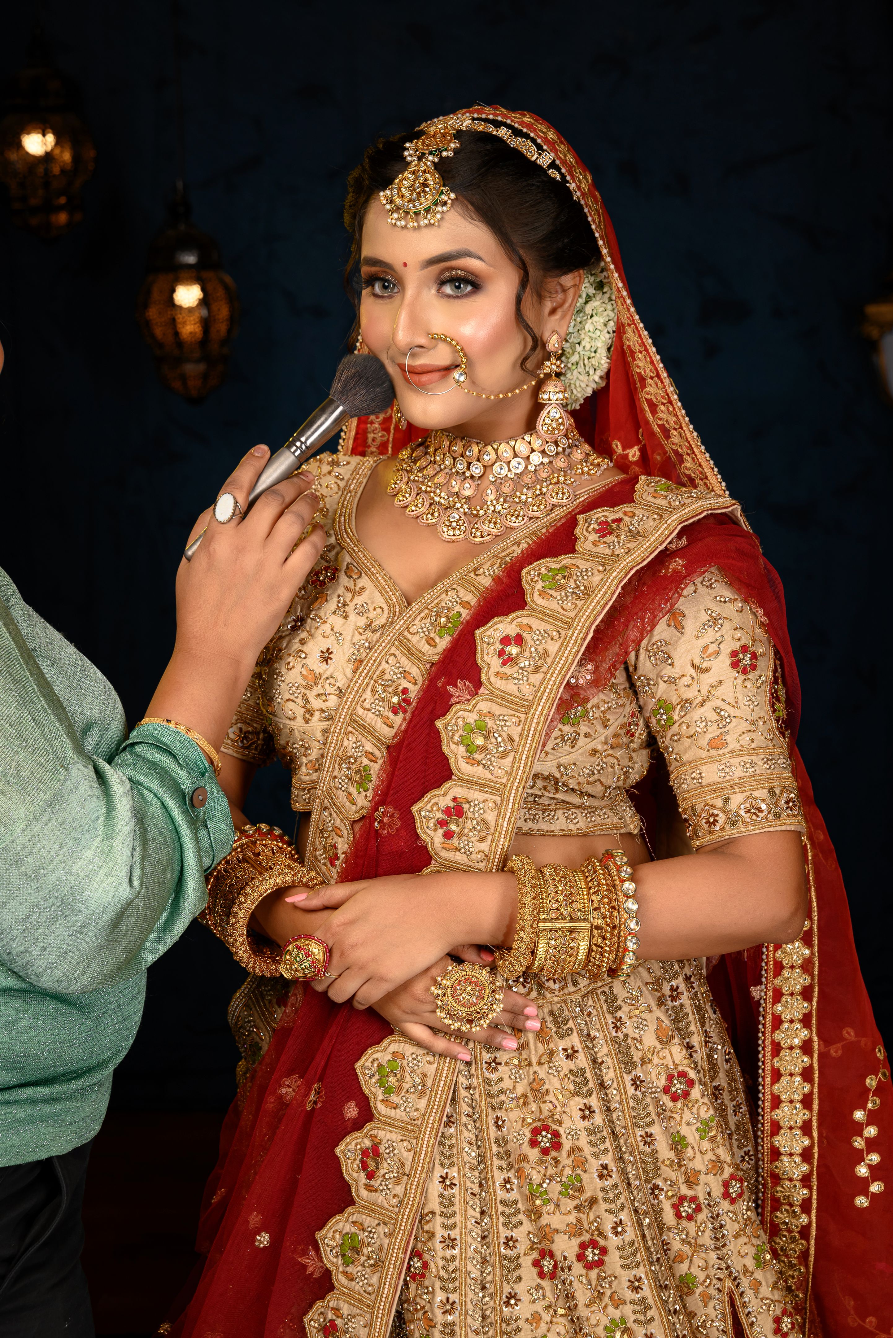 Stunning Indian bride dressed in traditional bridal lehenga with heavy gold jewellery and veil posing fashionable with makeup brush in studio lighting. Wedding fashion and lifestyle.