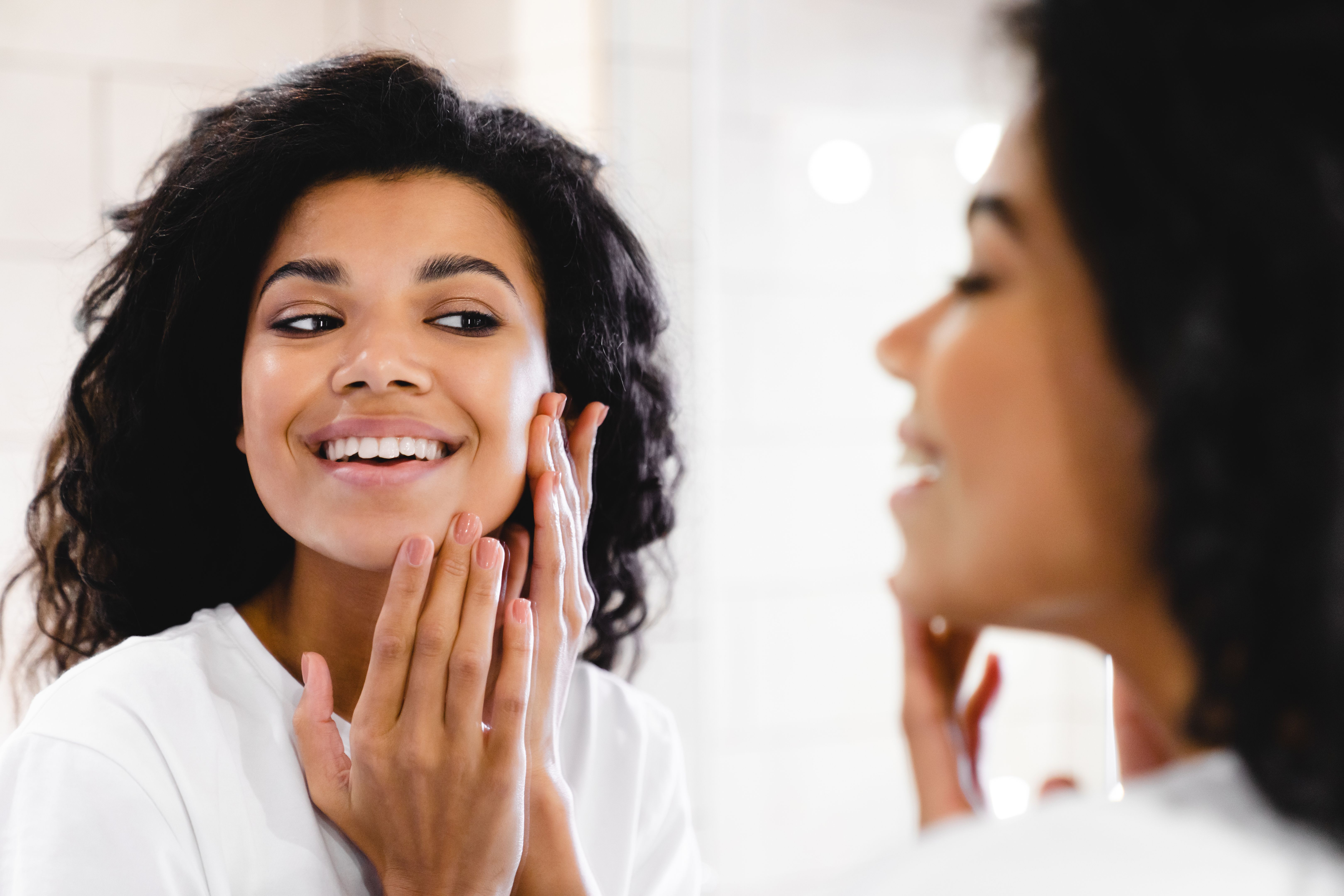 Pretty african young woman making beauty procedures with her face in the bathroom. African American woman look in mirror clean brush tooth in bathroom, young biracial female perform morning face care routine, do cleanup oral hygiene, use toothbrush