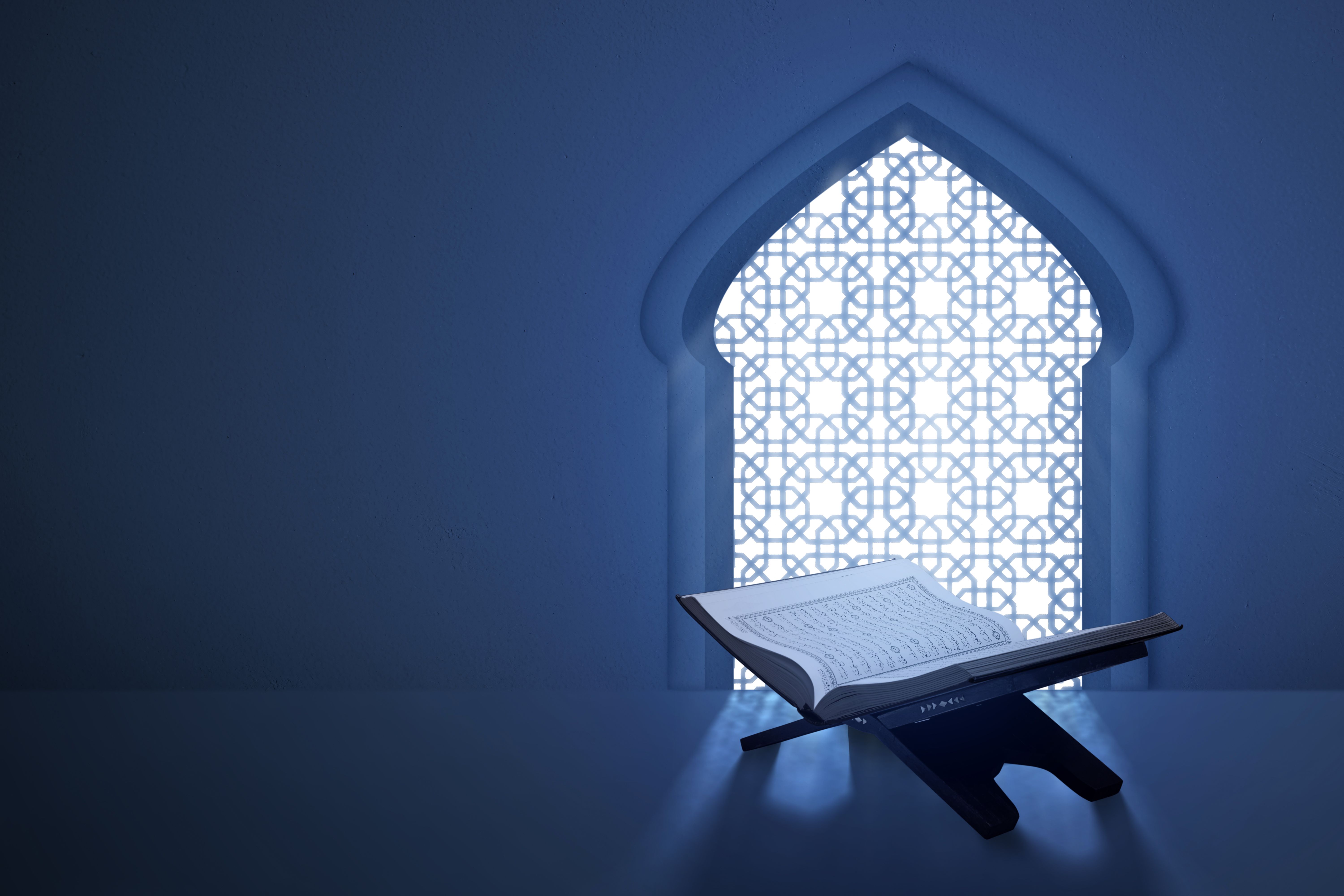 The opened holy book of Al Quran sitting with mosque window on the background. Muslim holy book
