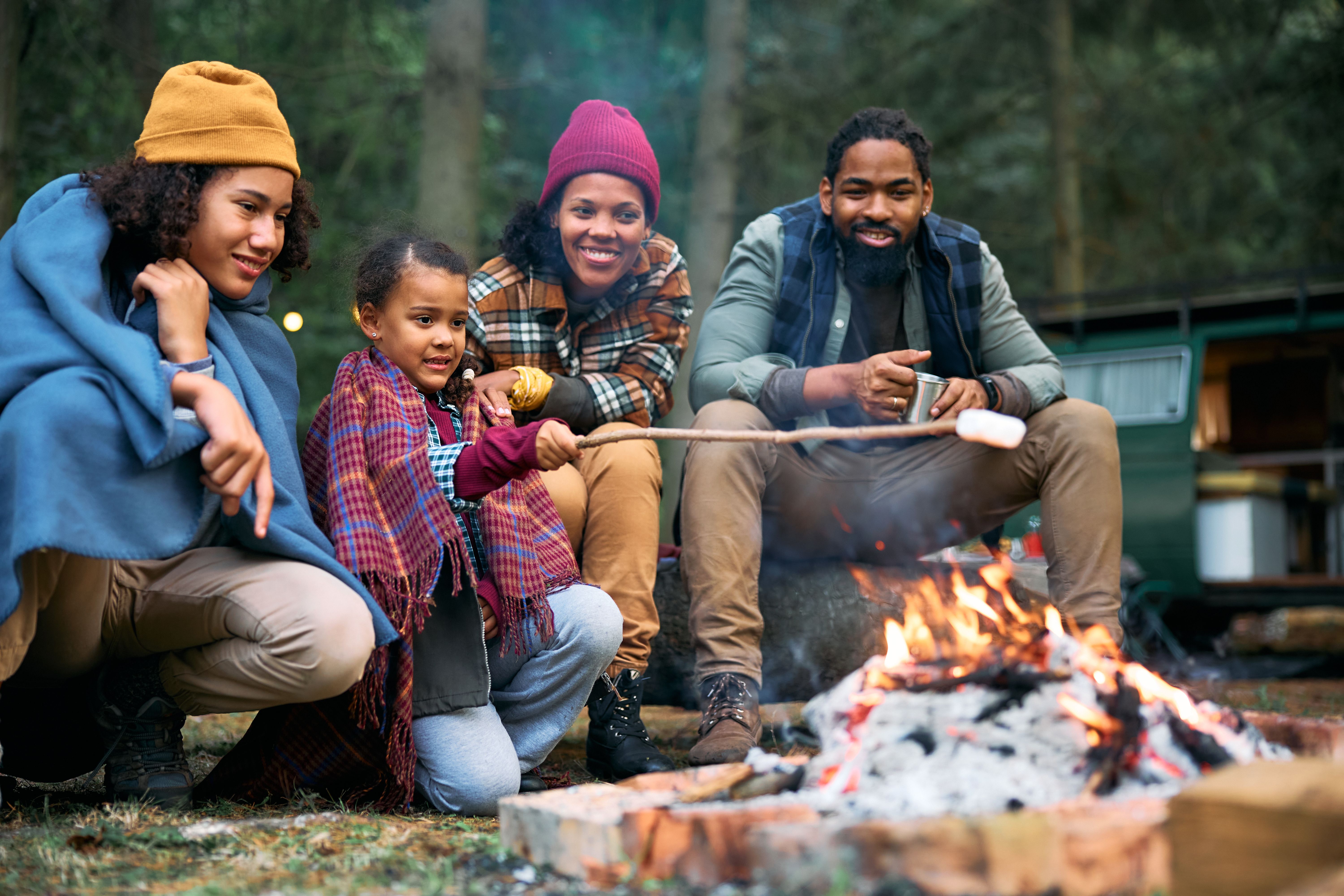 Happy black family roasting marshmallows while camping in the woods.