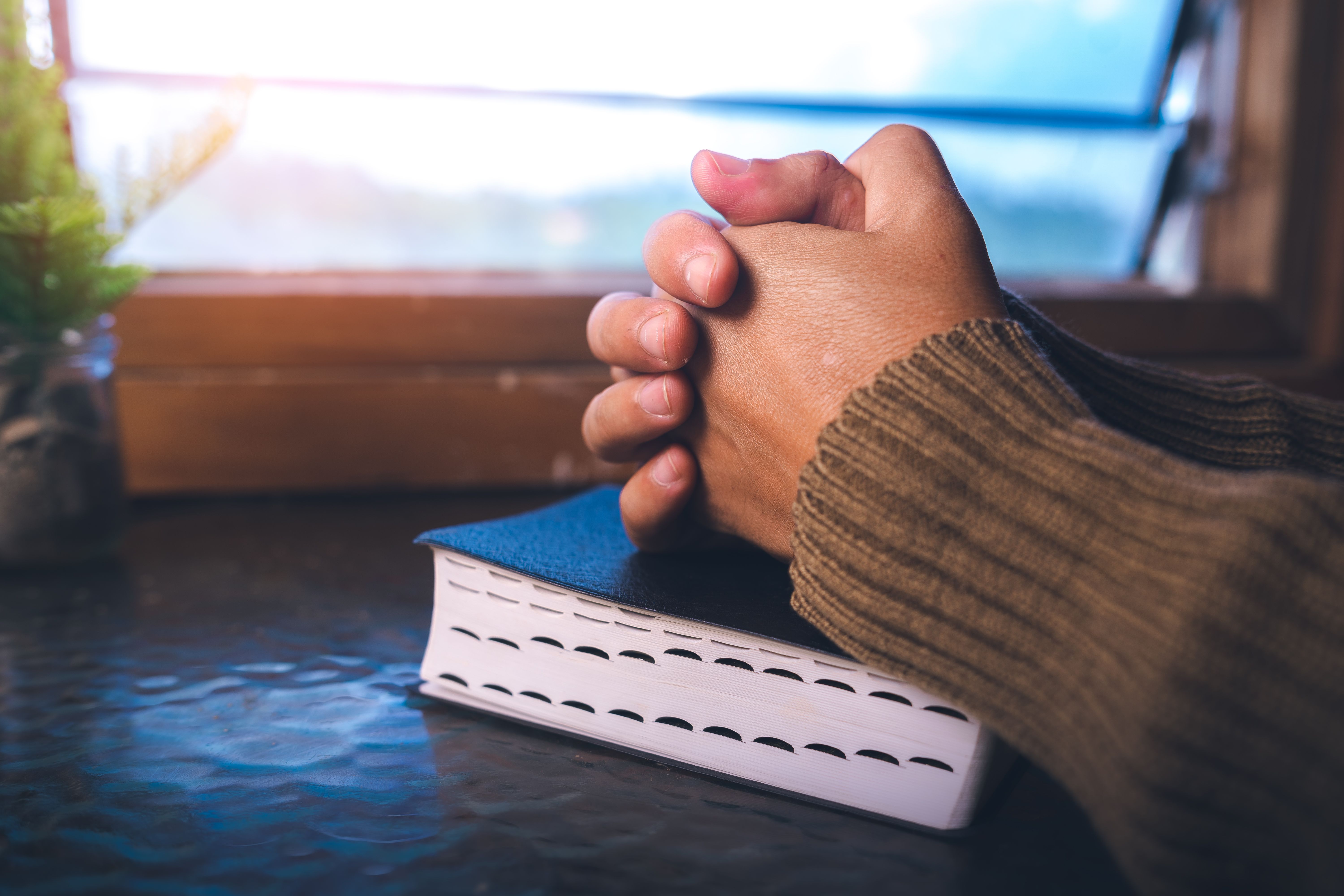 Close up of a man praying on bible at the window, christian background, devotional concept.