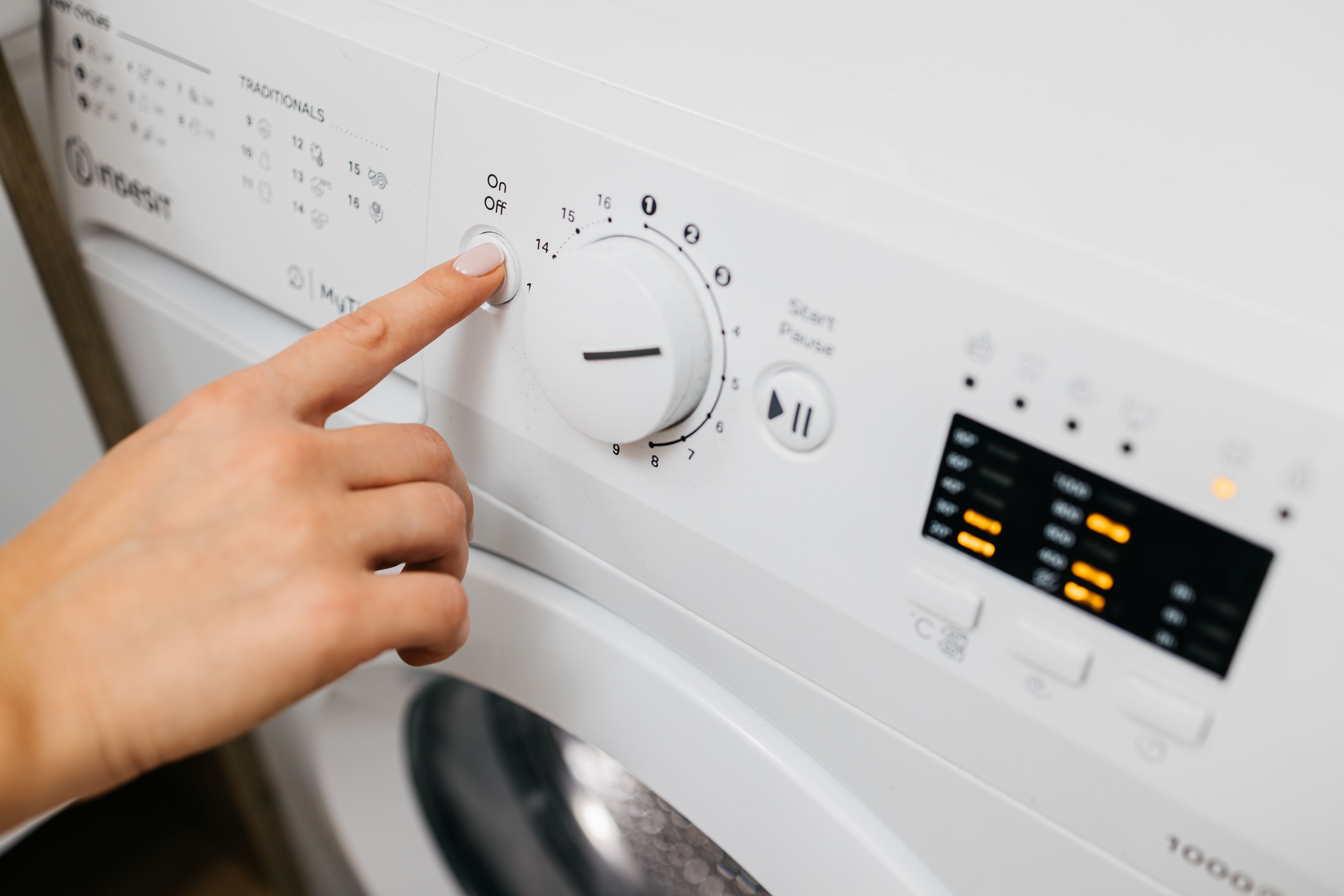 A woman loads dirty laundry into the washing machine and sets the wash cycle.