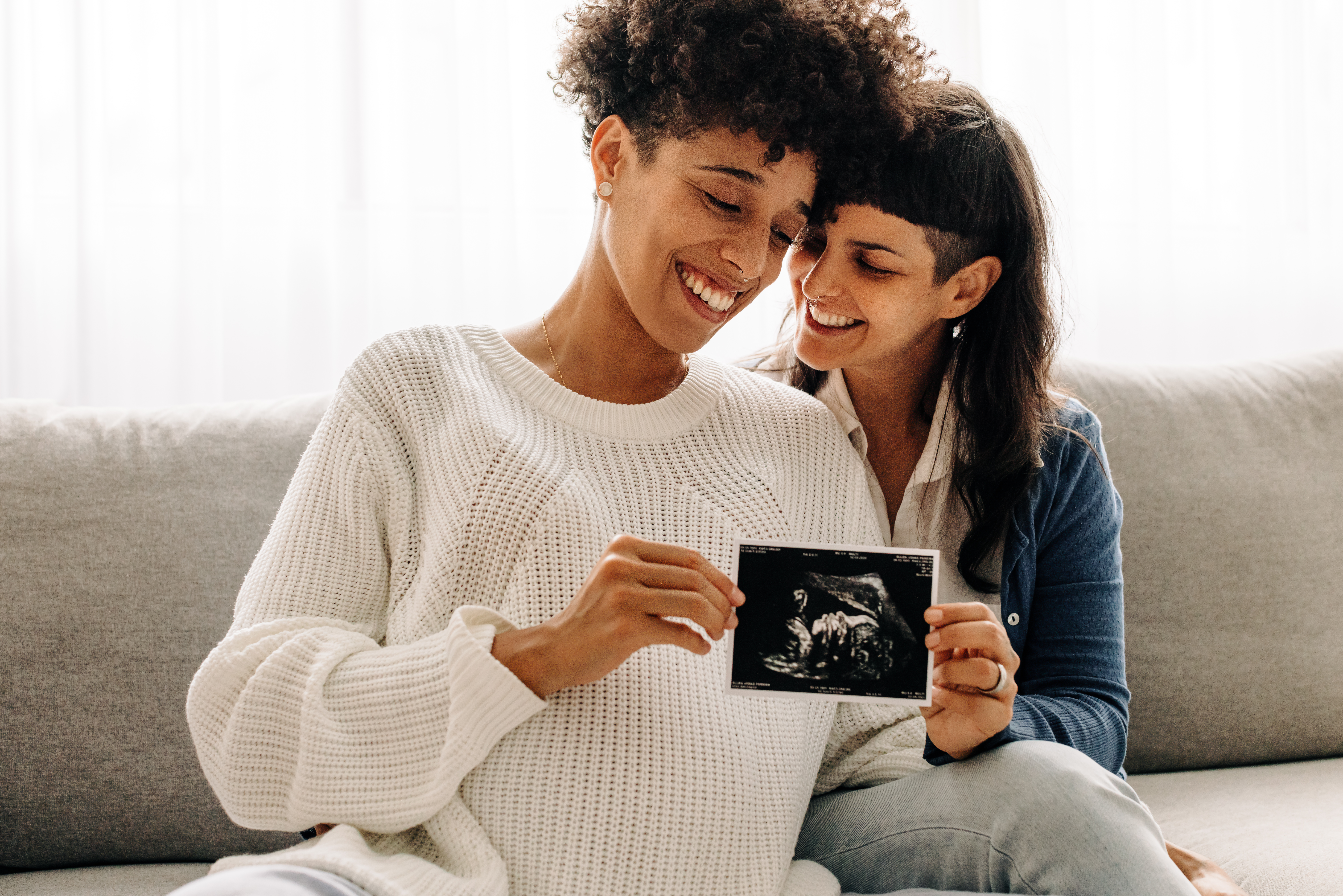 Same-sex pregnant couple holding up their ultrasound scan Same-sex pregnant couple holding up their ultrasound scan