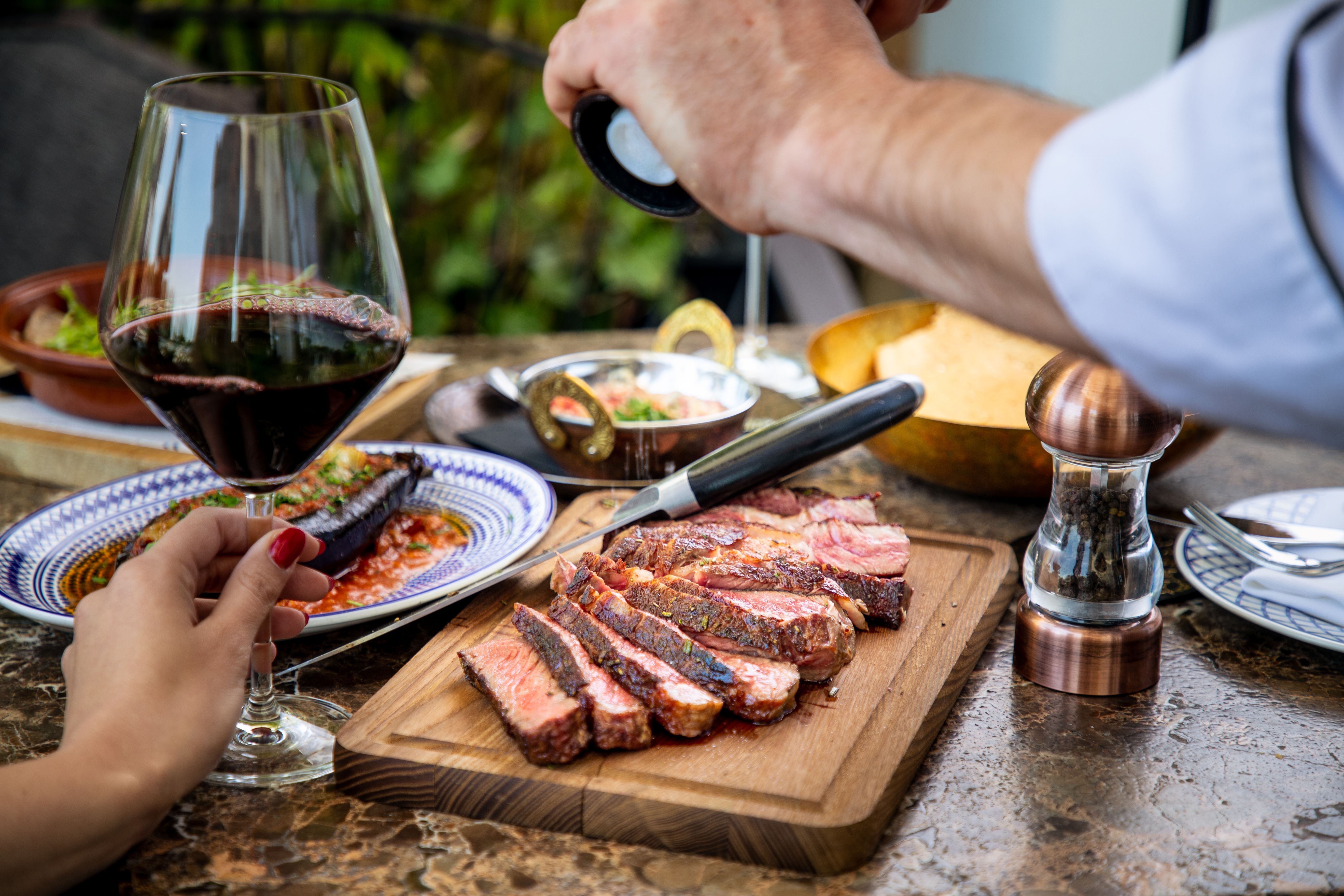 Seasoning medium rare steak with salt grinder, cut on wooden board on restaurant table