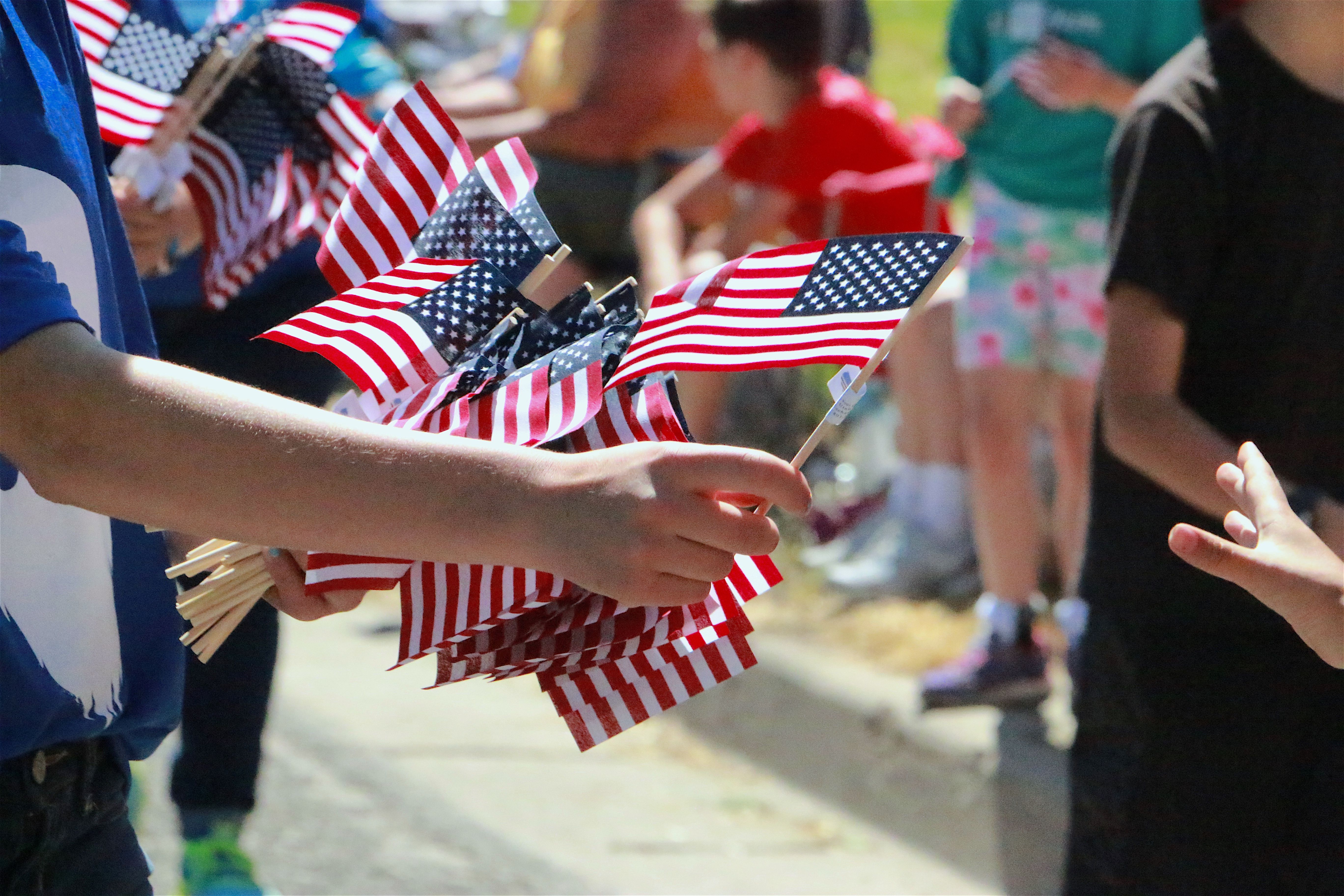 Closeup of male arm and hand passing out American Flags along parade route Blurred Crowd in Background •Veterans Day Celebration Phoenix Arizona Closeup of male arm and hand passing out American Flags along parade route Blurred Crowd in Background •Veterans Day Celebration Phoenix Arizona