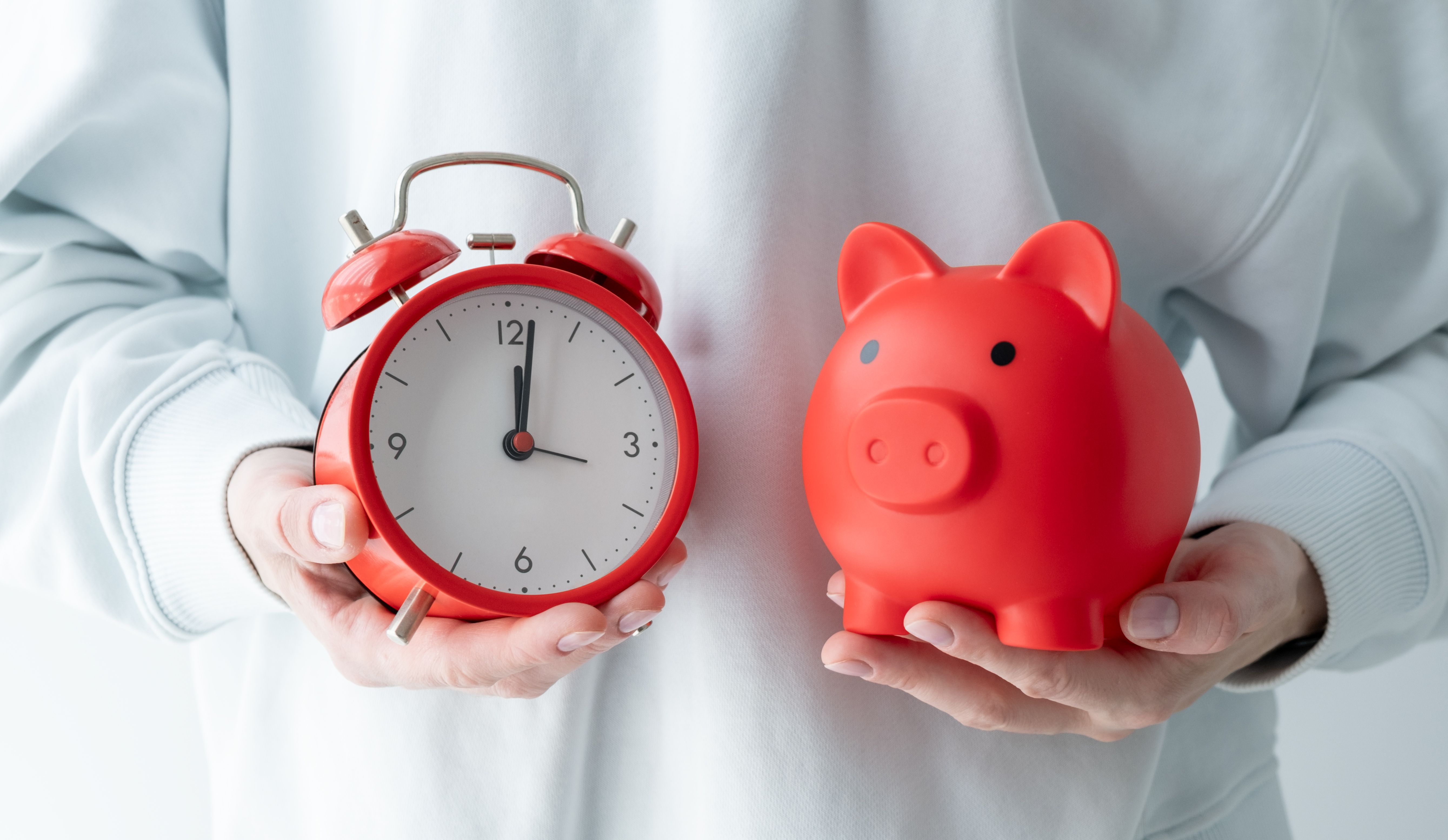 A person holding a red piggy bank and a red alarm clock