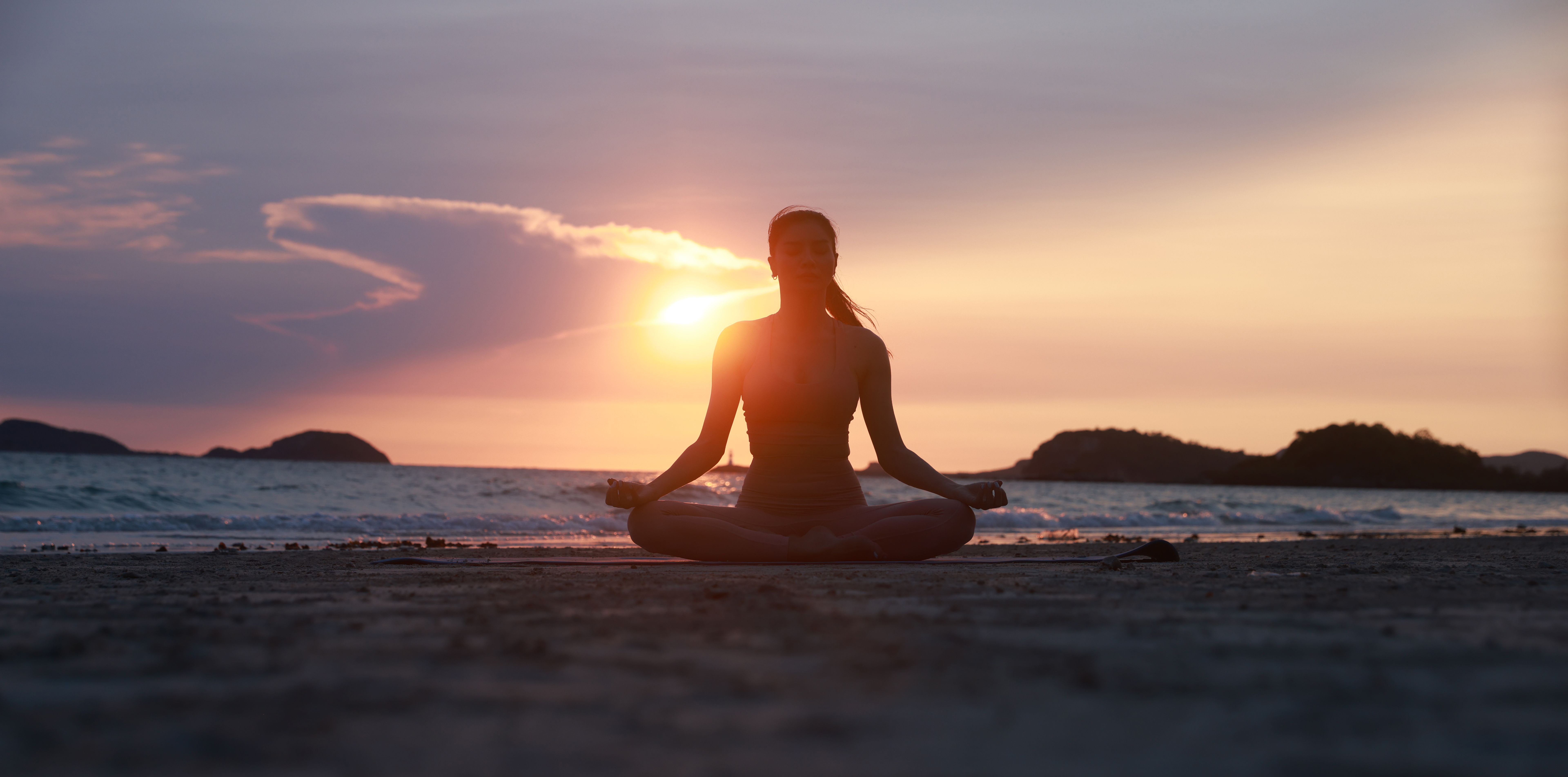Experience the serene beauty of yoga on the beach at sunset, with a silhouette of a woman stretching her arms and legs