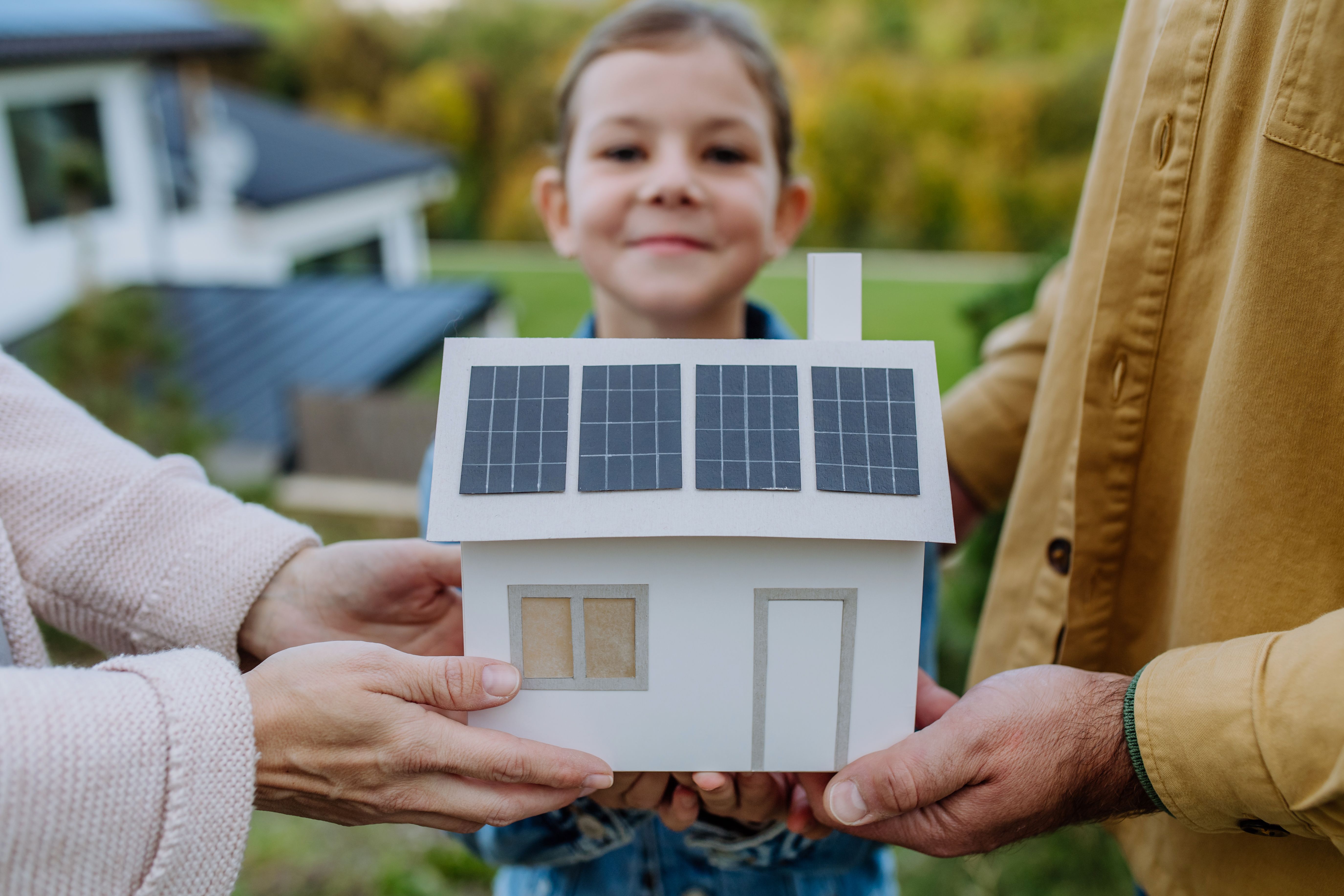 Primo piano di una giovane famiglia che tiene in mano un modello di carta di casa con pannelli solari. Energia alternativa, risparmio di risorse e concetto di stile di vita sostenibile.