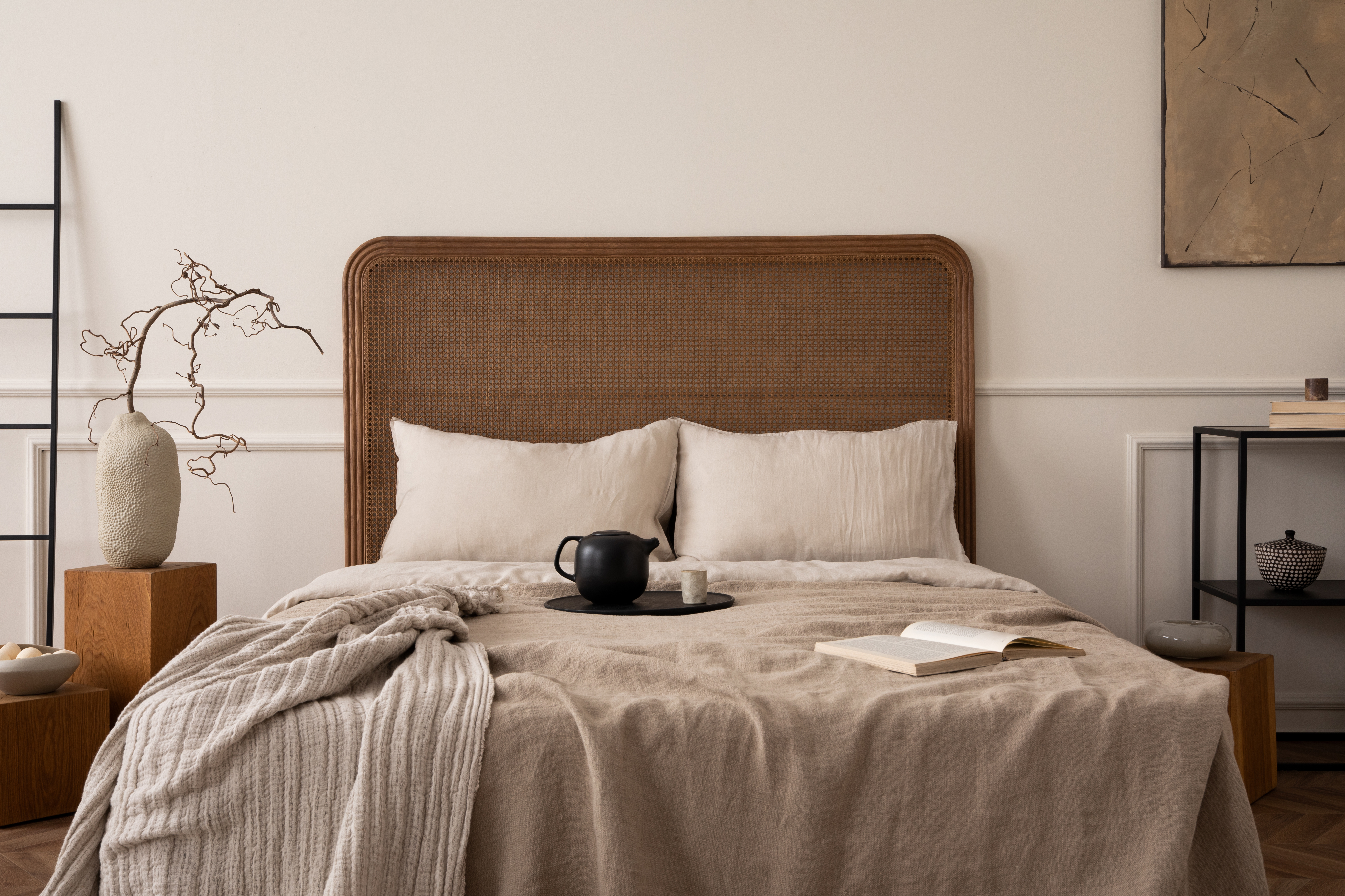 Composición creativa del interior del dormitorio con cama acogedora, ropa de cama beige, cuadros, trazo con jarra y taza, mesa de centro con rama, escalera negra y accesorios personales. Decoración del hogar. Plantilla.