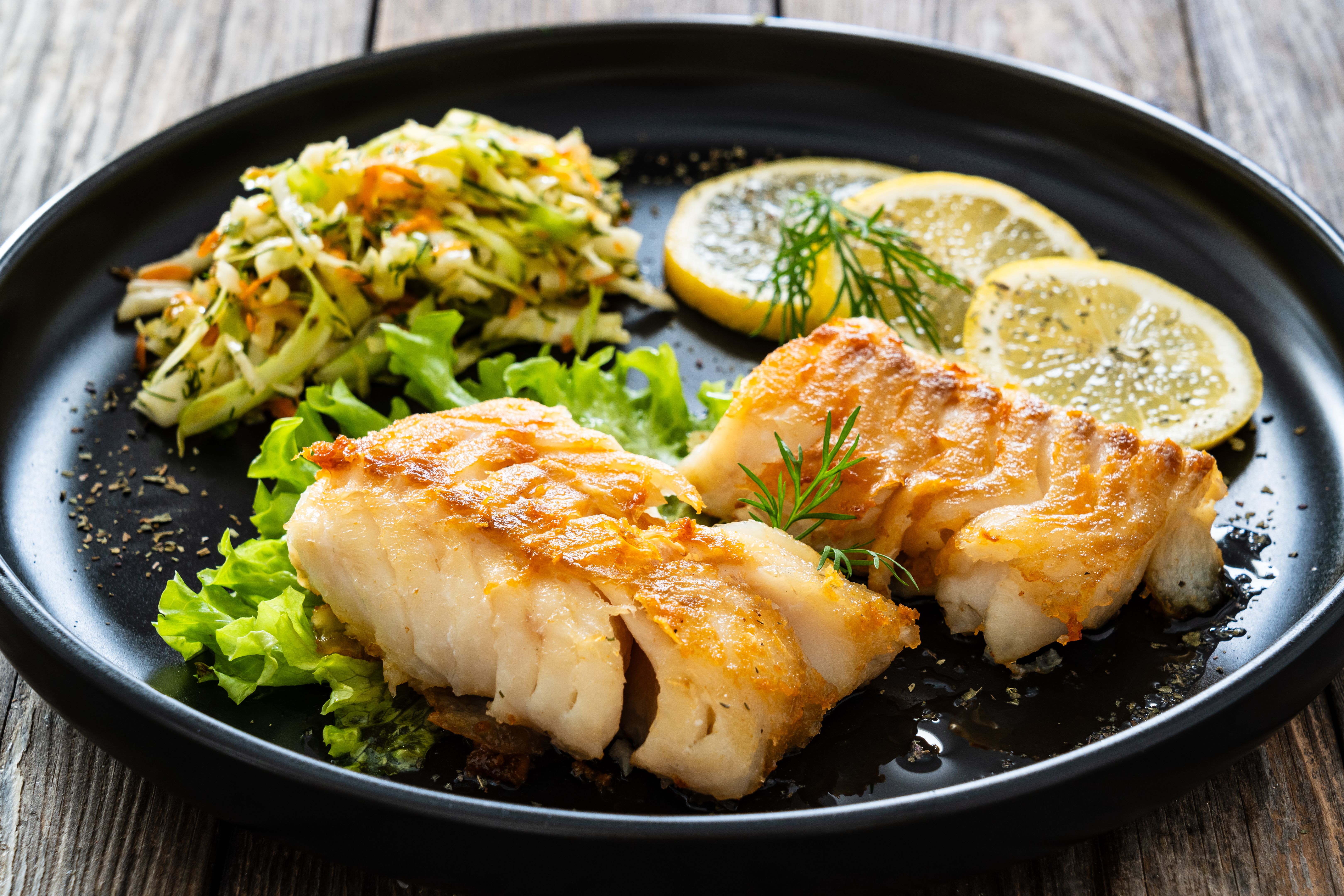 Fried codfish fillet and cabbage salad served on wooden table