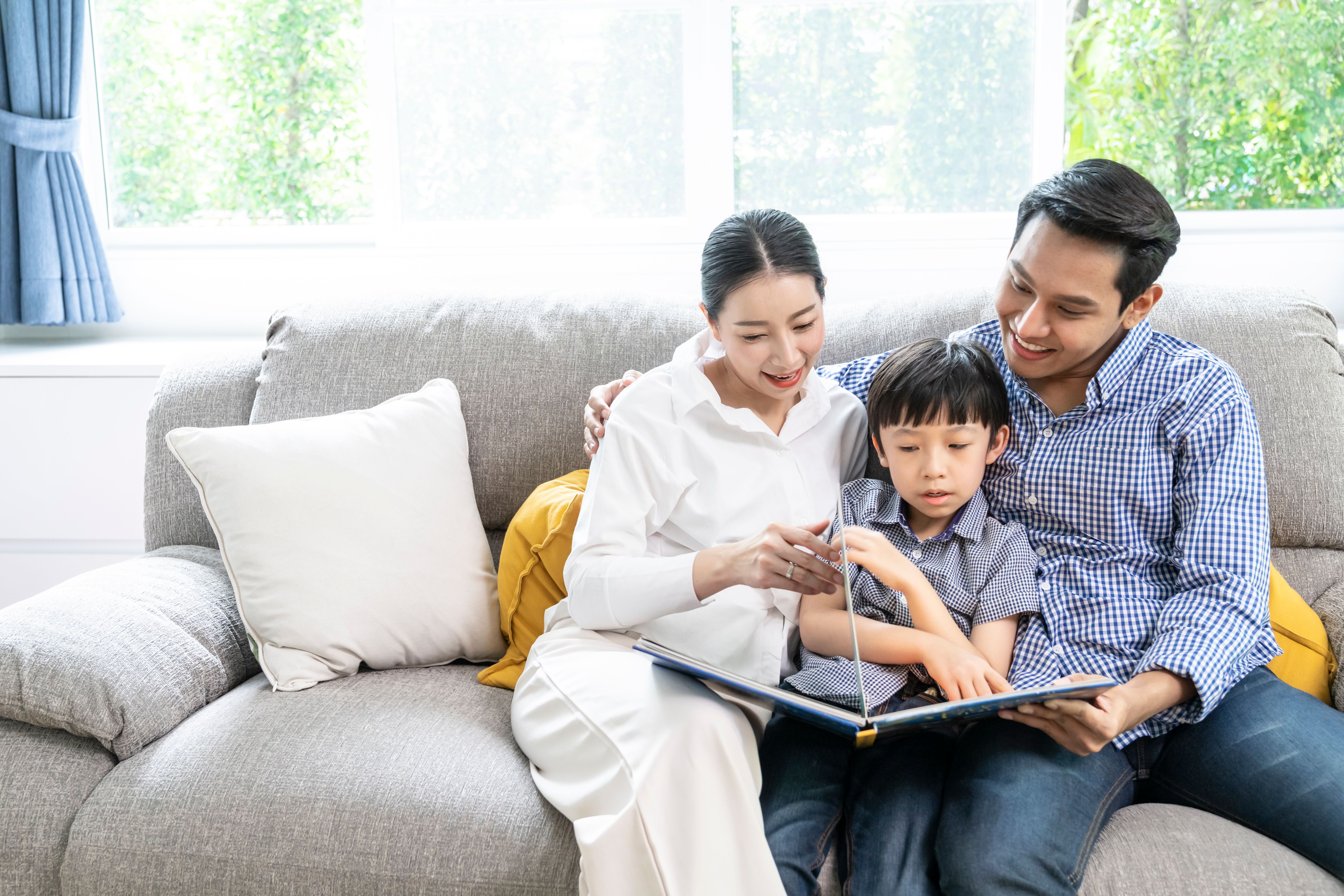 The parents and child read a book together in the living room