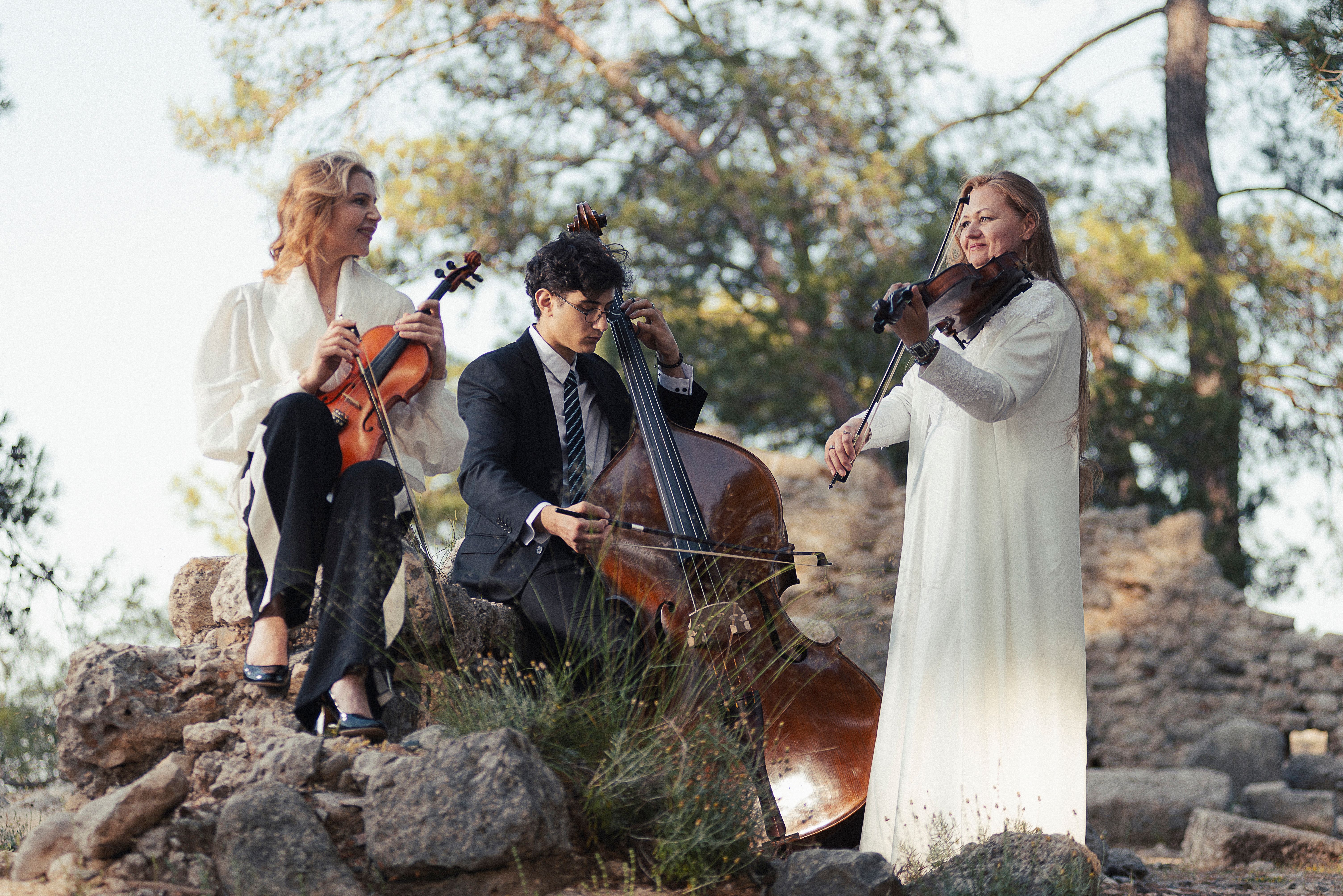 Two musicians in white dress and one musician in black suit in the forest.