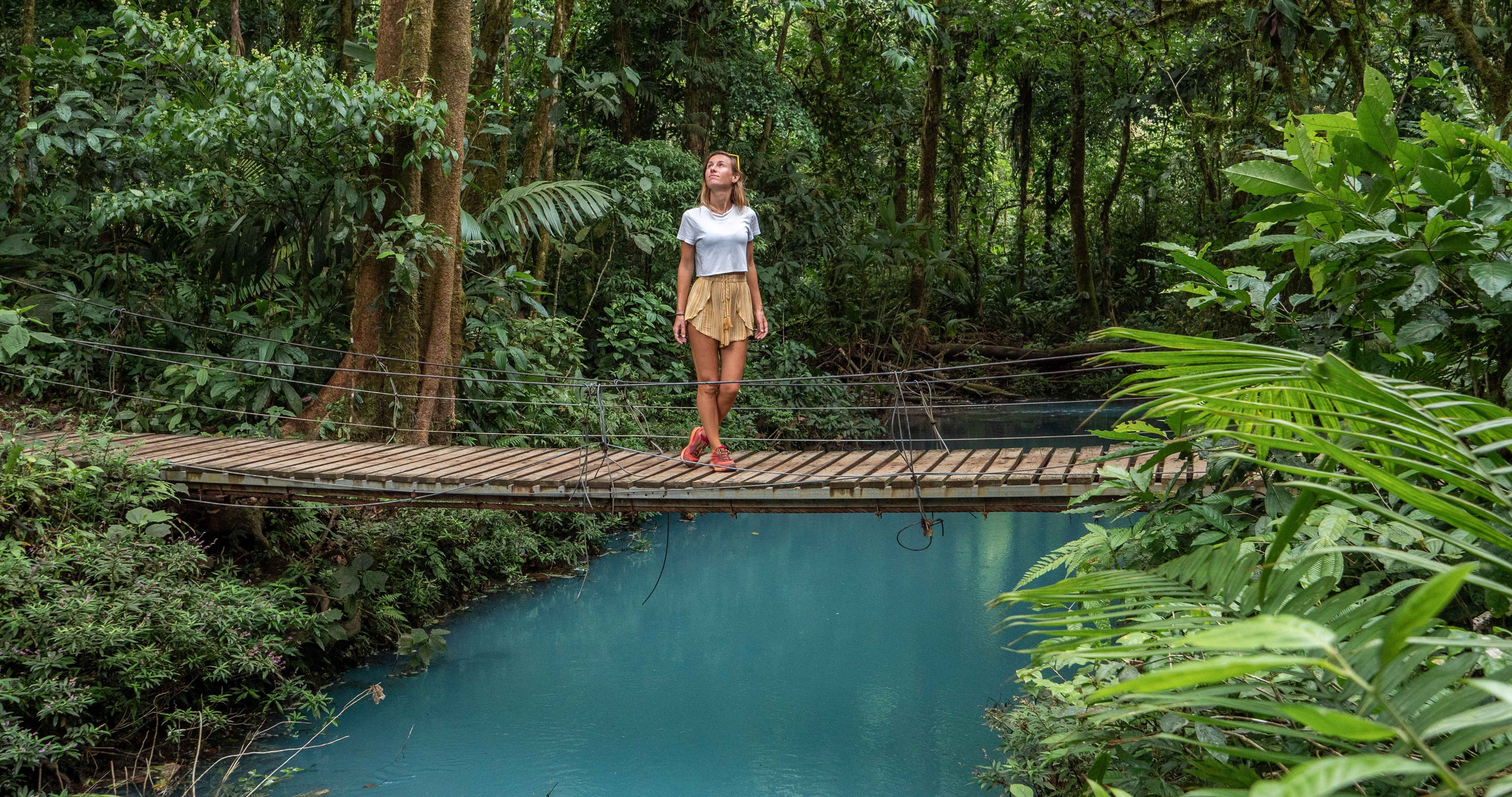 Young woman wandering in tropical rainforest walking on bridge over turquoise lagoon