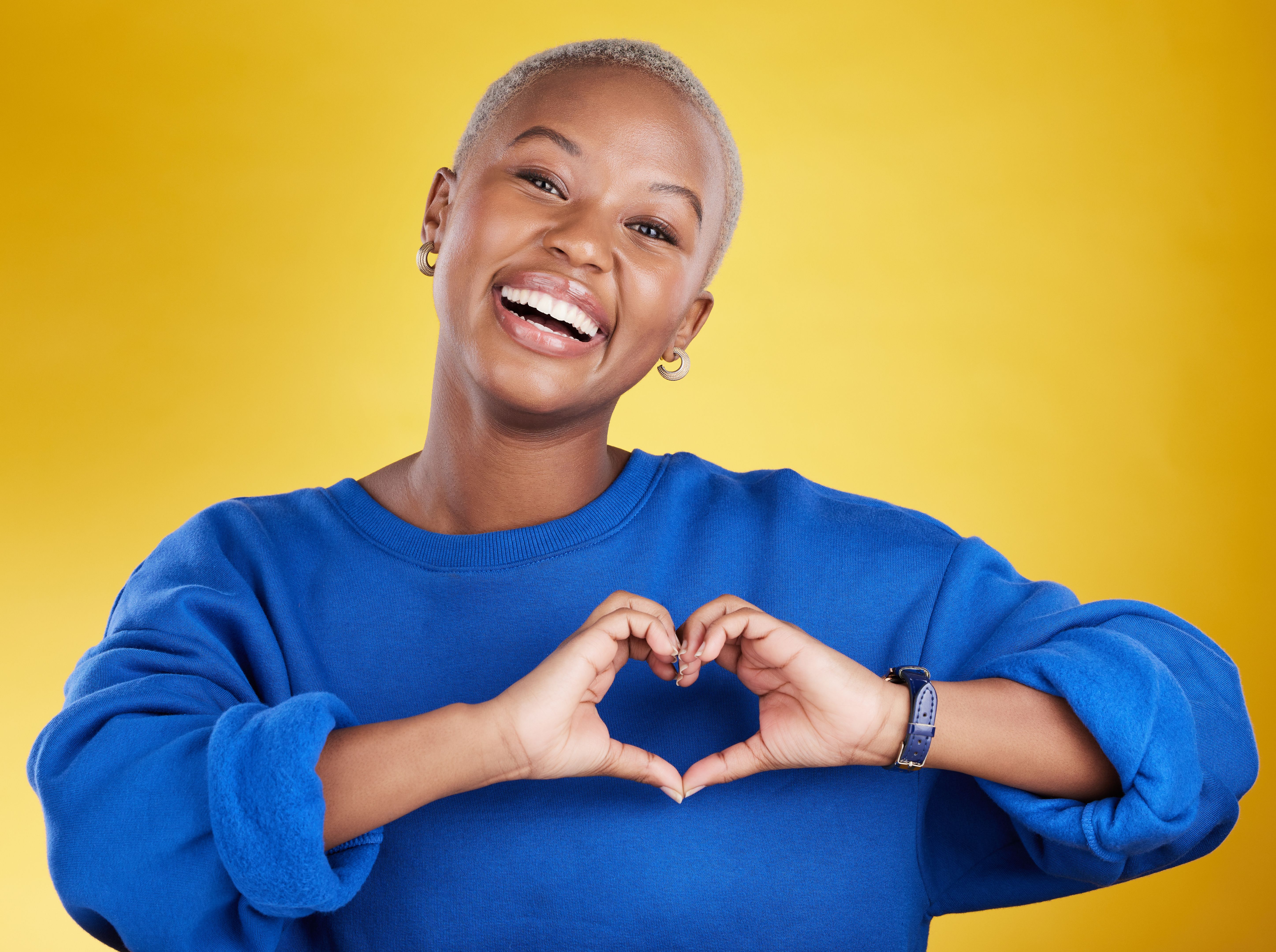 Heart hands, portrait and happy black woman in studio, background and color backdrop for emoji. Smile, female model and finger shape for love, thank you and support of peace, care or sign of kindness