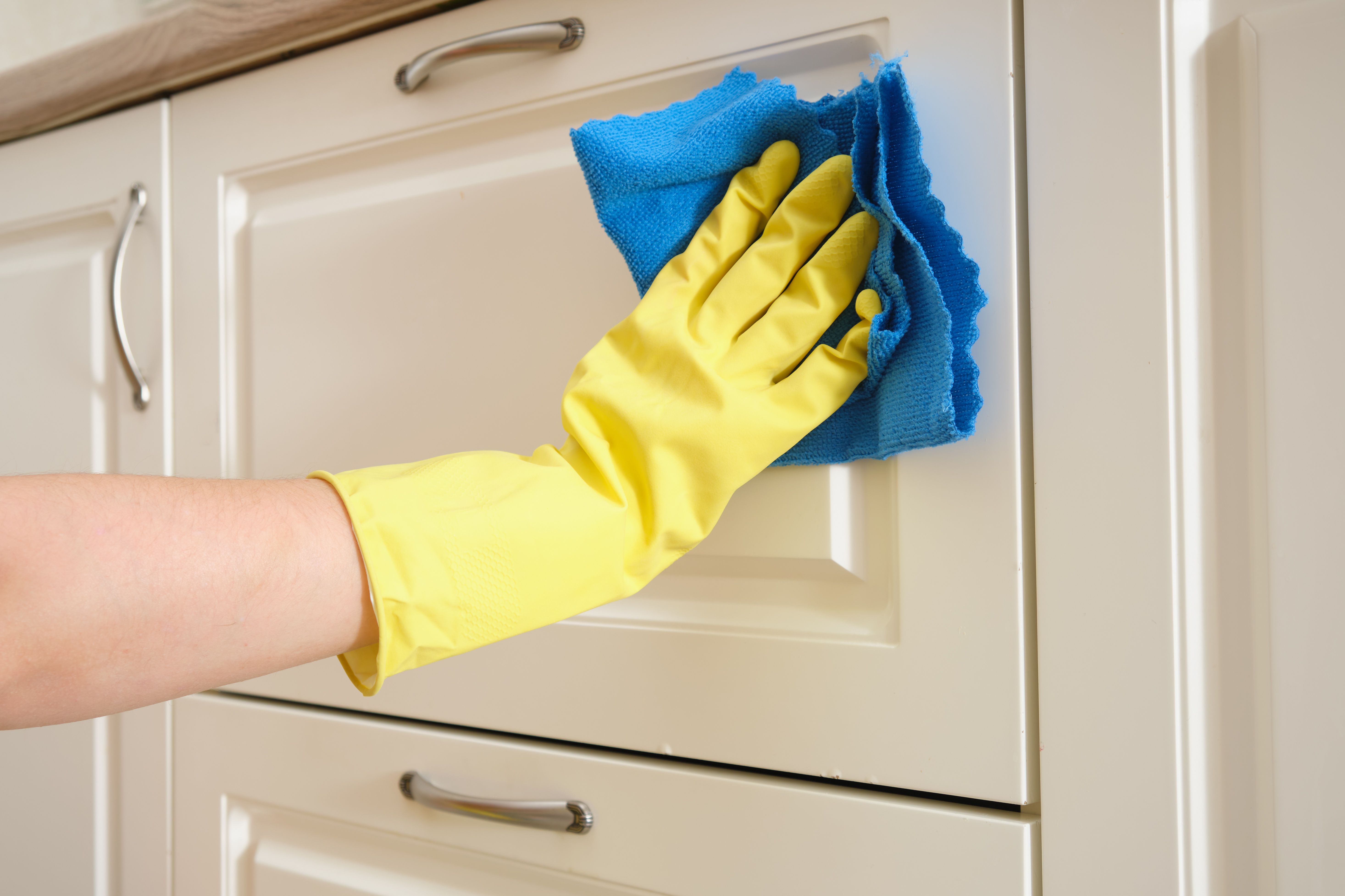 A woman washes furniture in her home kitchen with a blue cloth. Female hands in yellow gloves while cleaning the kitchen A woman washes furniture in her home kitchen with a blue cloth. Female hands in yellow gloves while cleaning the kitchen