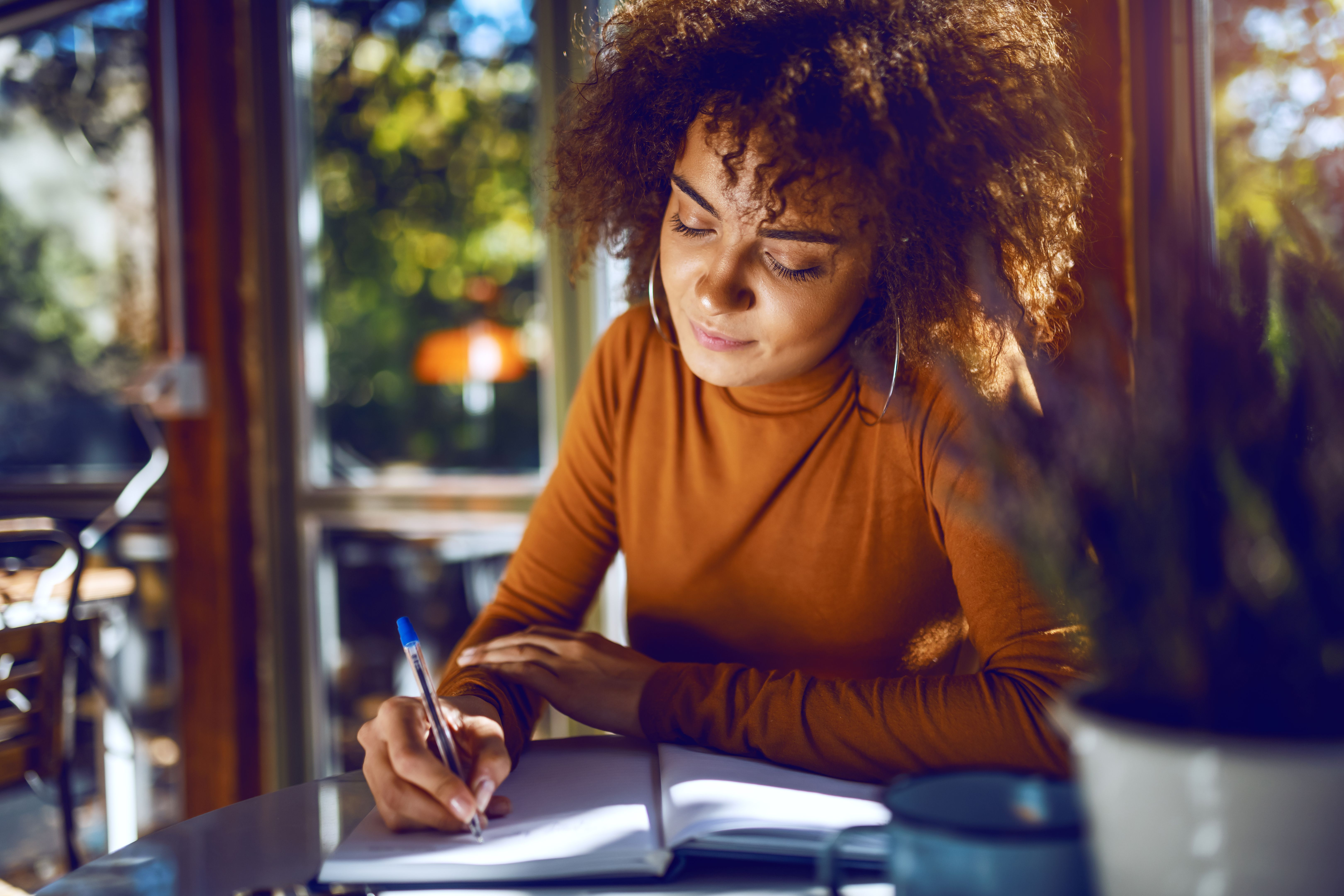 Portrait of cute mixed race student with curly hair and in turtleneck sitting in cafe and studying for exams. Portrait of cute mixed race student with curly hair and in turtleneck sitting in cafe and studying for exams.