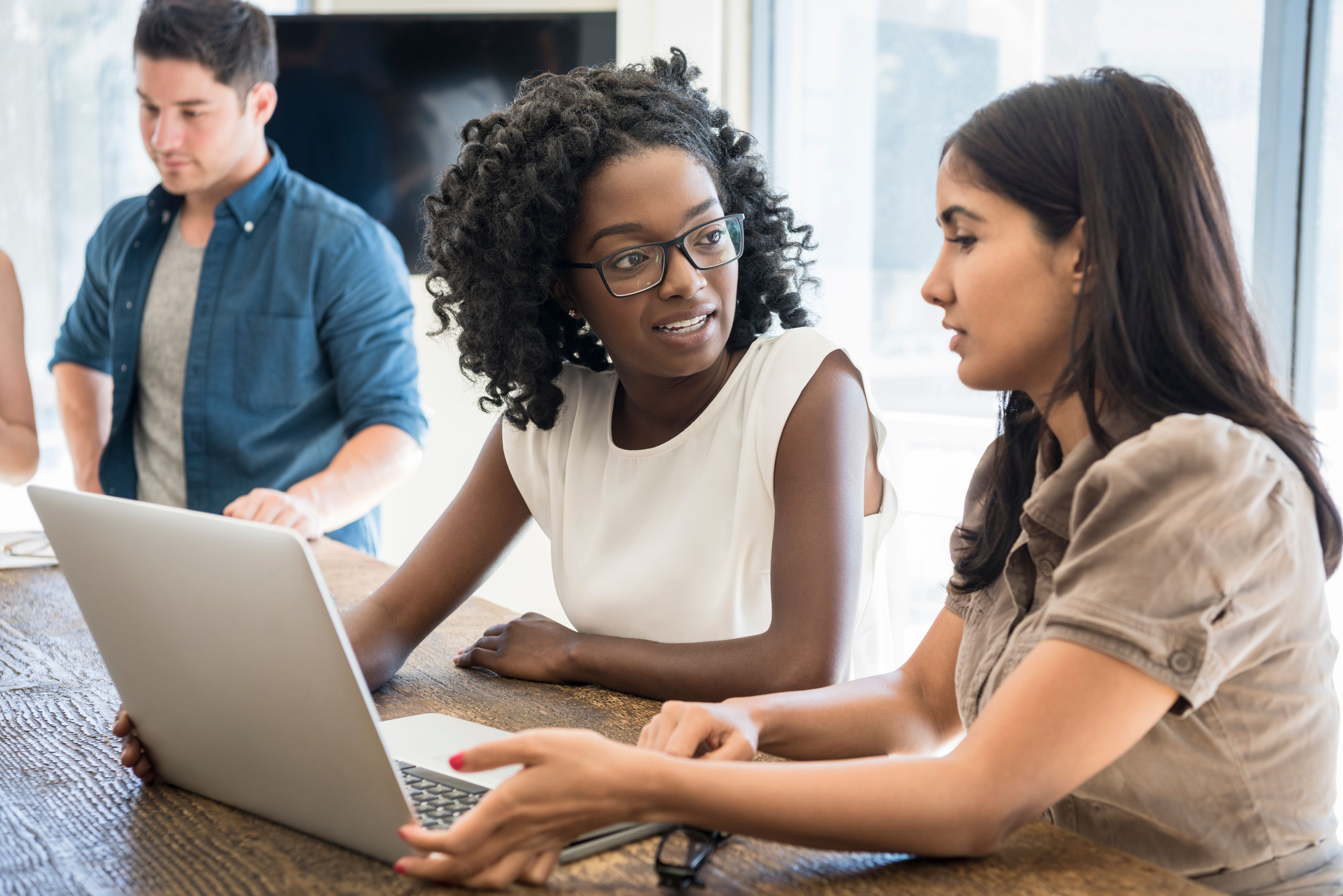 Two young businesswomen using laptop at work with serious expressions